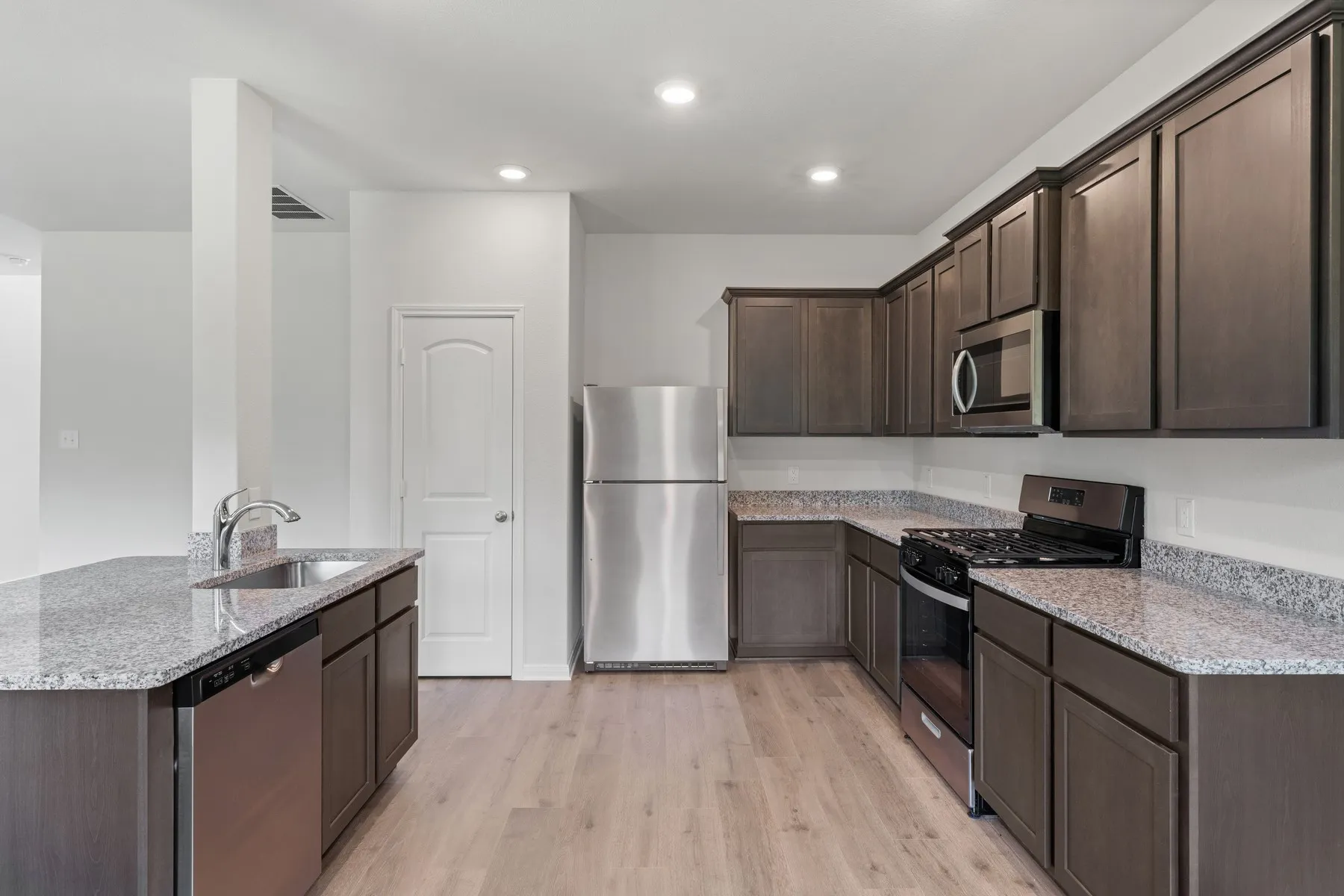 Kitchen featuring stainless steel appliances, dark brown cabinetry, light stone counters, light wood-type flooring, and recessed lighting