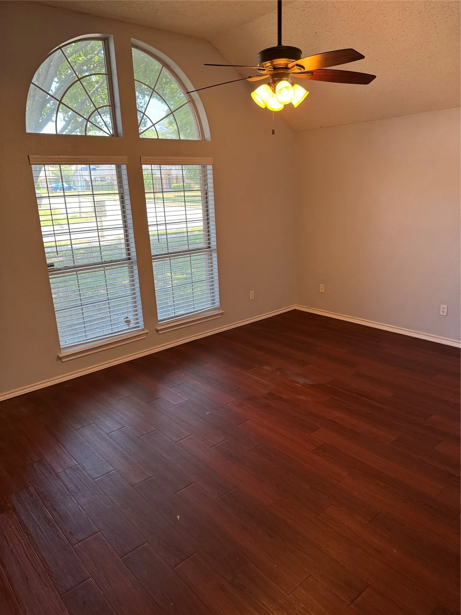 Empty room with a textured ceiling, lofted ceiling, ceiling fan, and dark wood-type flooring