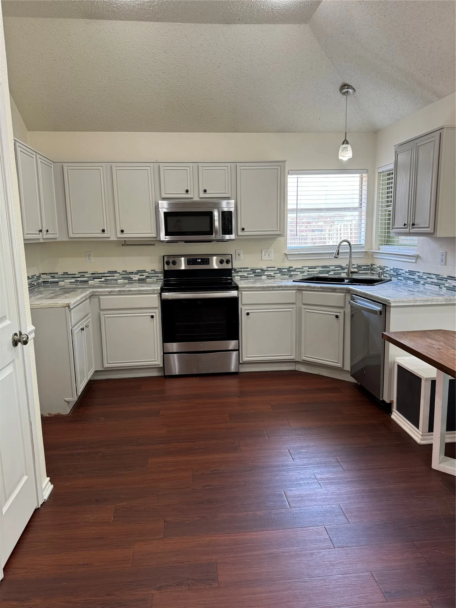 Kitchen with sink, dishwasher, dark wood-type flooring, hanging light fixtures, and stainless steel range with electric stovetop