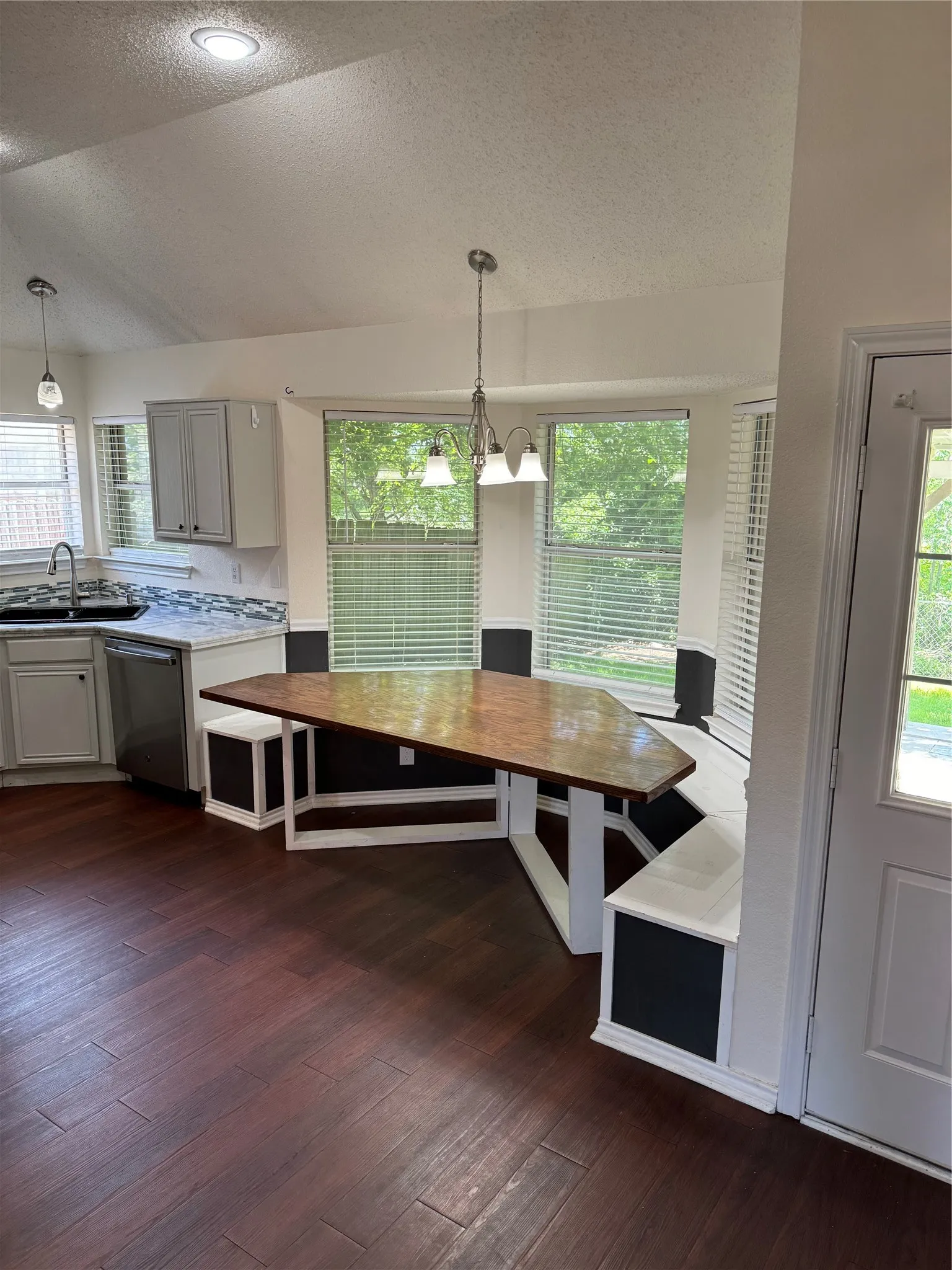 Unfurnished dining area featuring a textured ceiling, sink, dark hardwood / wood-style floors, vaulted ceiling, and an inviting chandelier