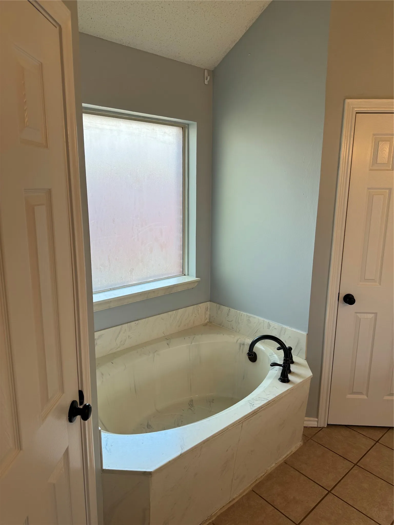 Bathroom with a bath to relax in, a textured ceiling, and tile flooring