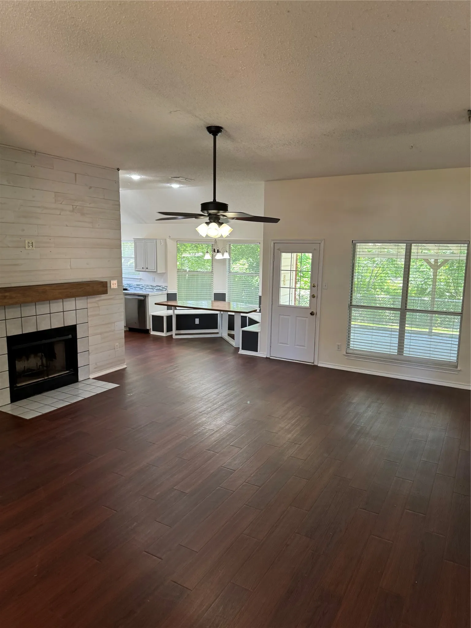 Unfurnished living room with a textured ceiling, dark hardwood / wood-style flooring, ceiling fan, and a tiled fireplace