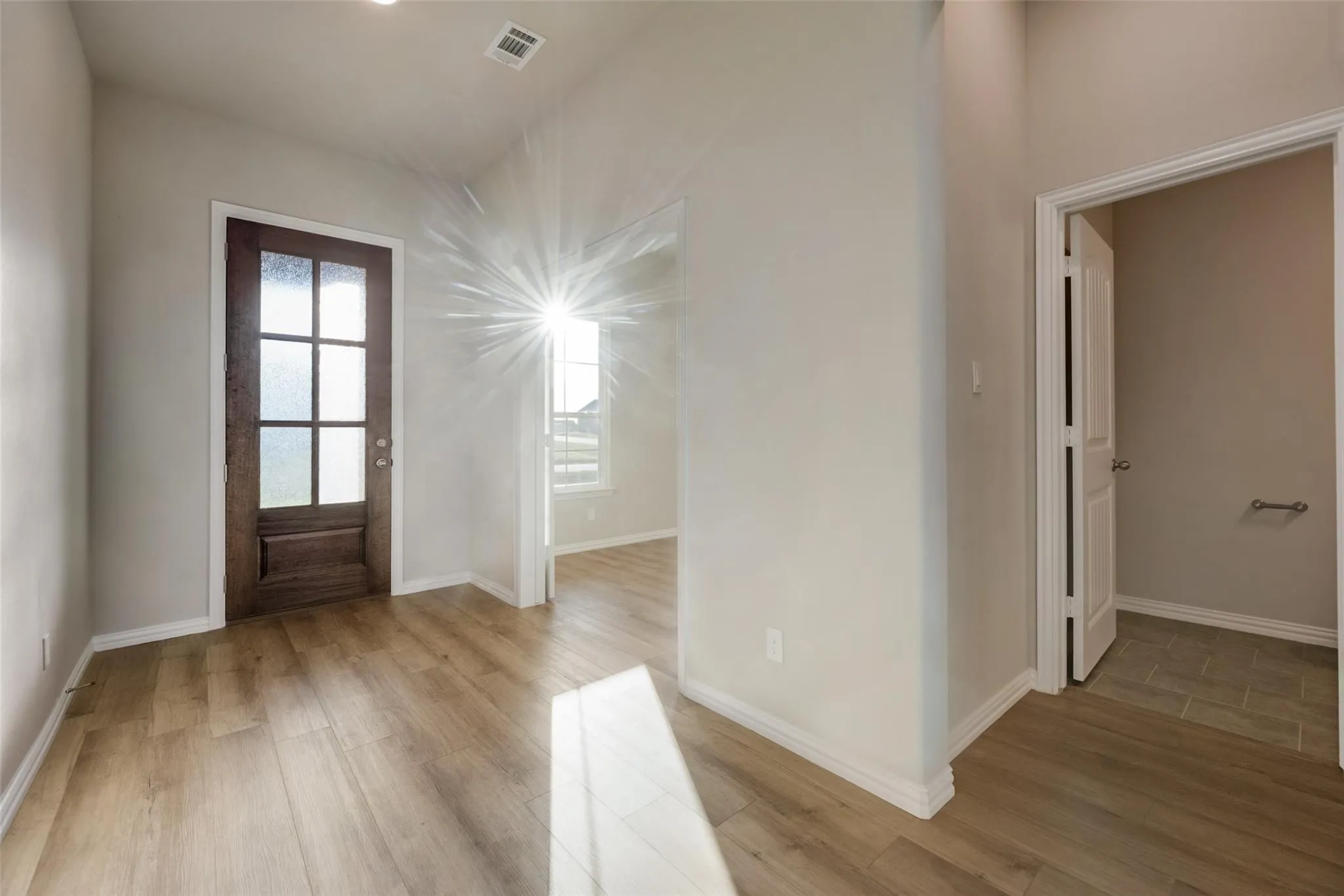 Vaulted ceiling, recessed lighting, wood-finish flooring, paneled entry door with frosted glass, and white trim