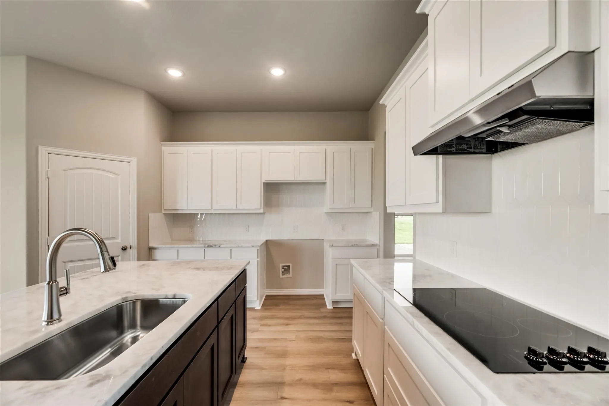 Kitchen featuring a large island with an undermount sink, light-toned countertops, white cabinetry, a white subway tile backsplash, and wood-finish flooring