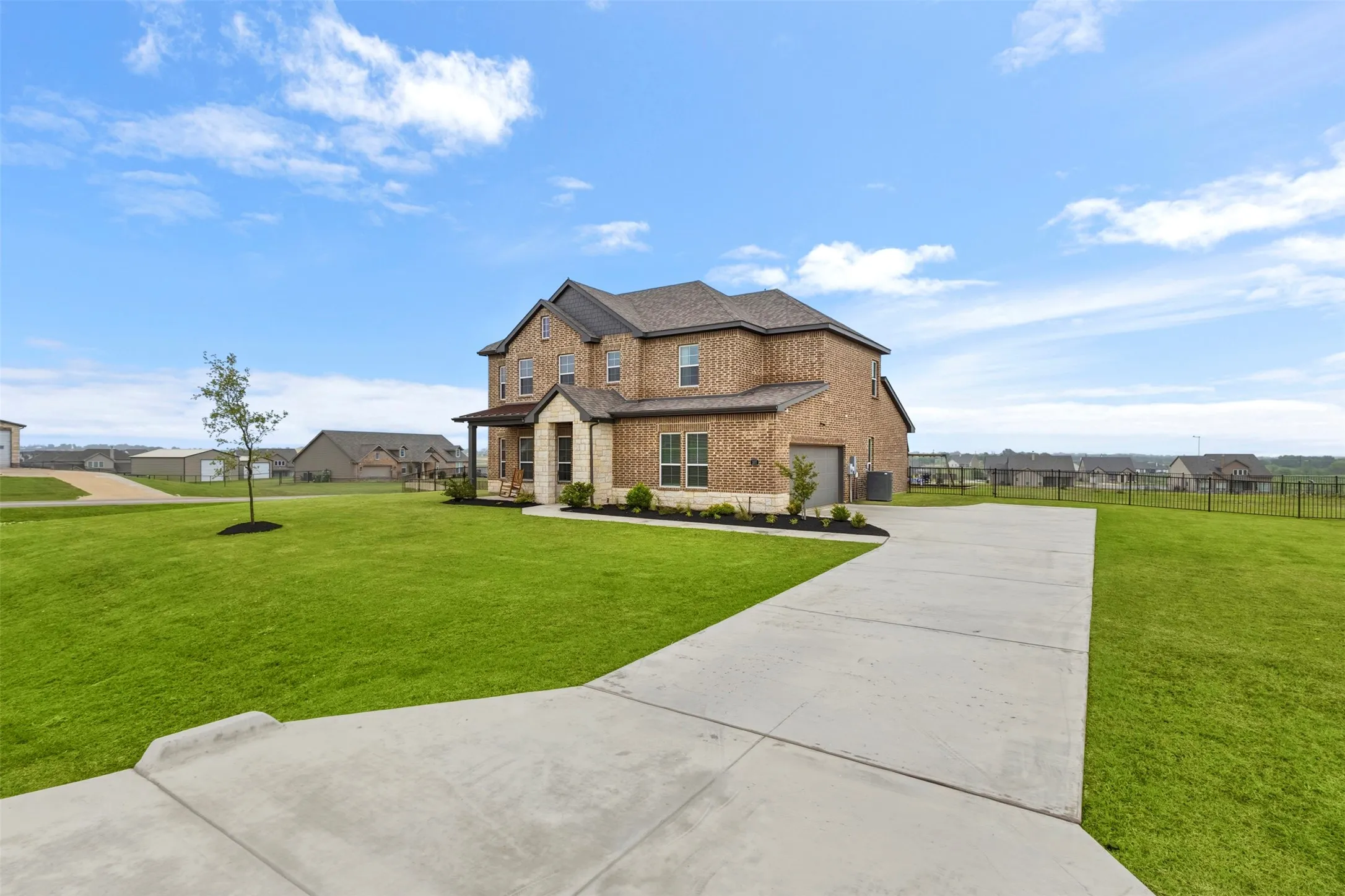 Brick exterior with stone accents, covered porch, attached garage, concrete driveway, and expansive lawn