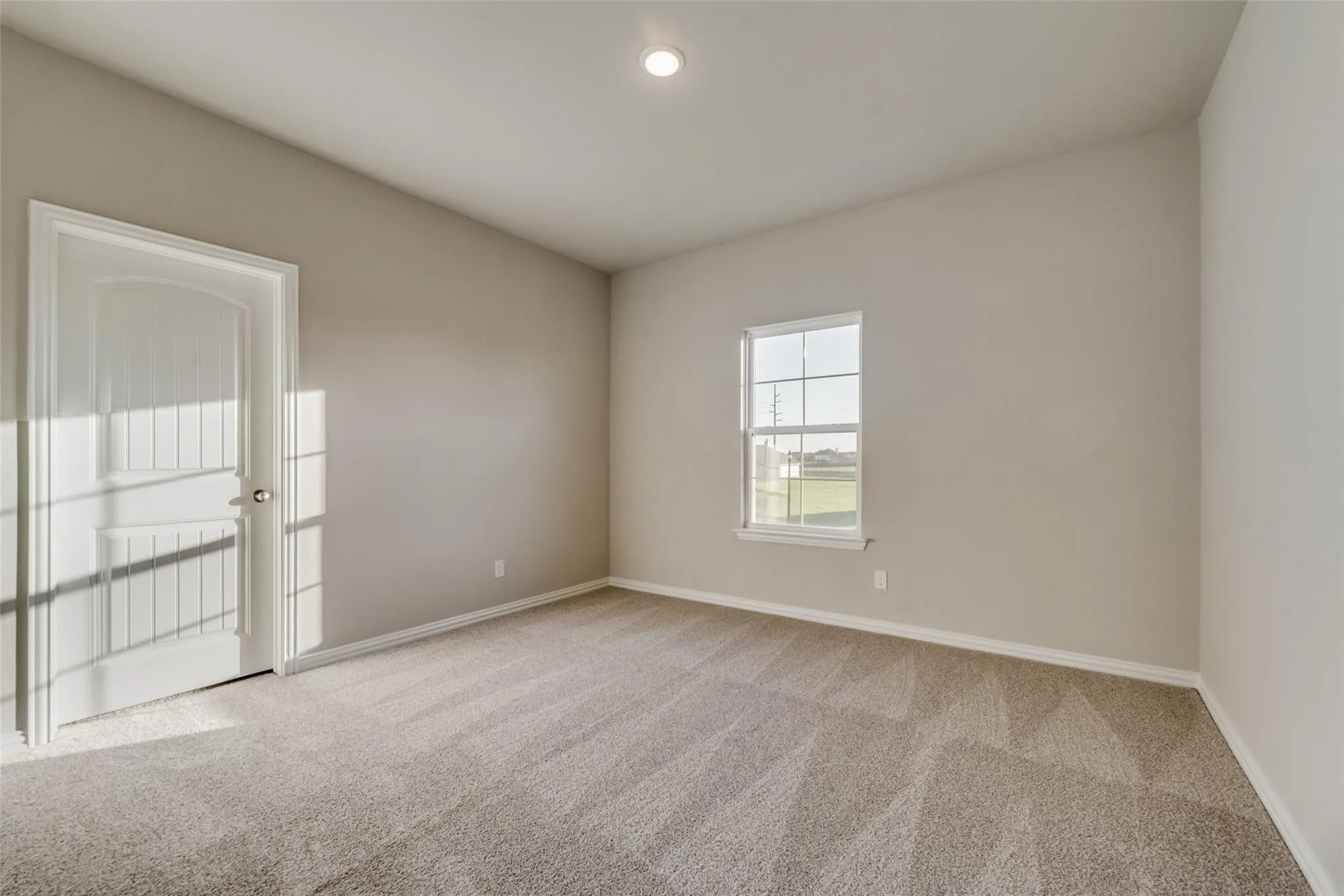Recessed ceiling lighting, neutral carpet, white trim, single window, and a paneled door