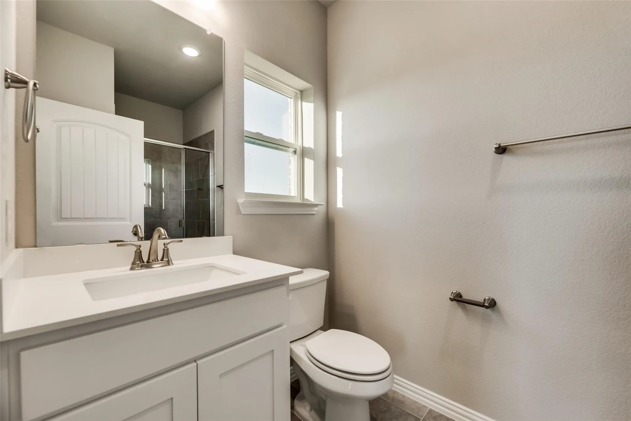 White vanity with an integrated sink, brushed nickel faucet, large mirror, and tiled flooring