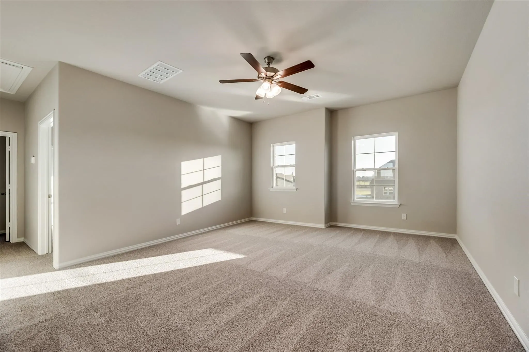 Spacious room featuring carpeting, multiple windows, a ceiling fan with integrated lighting, and neutral wall tones