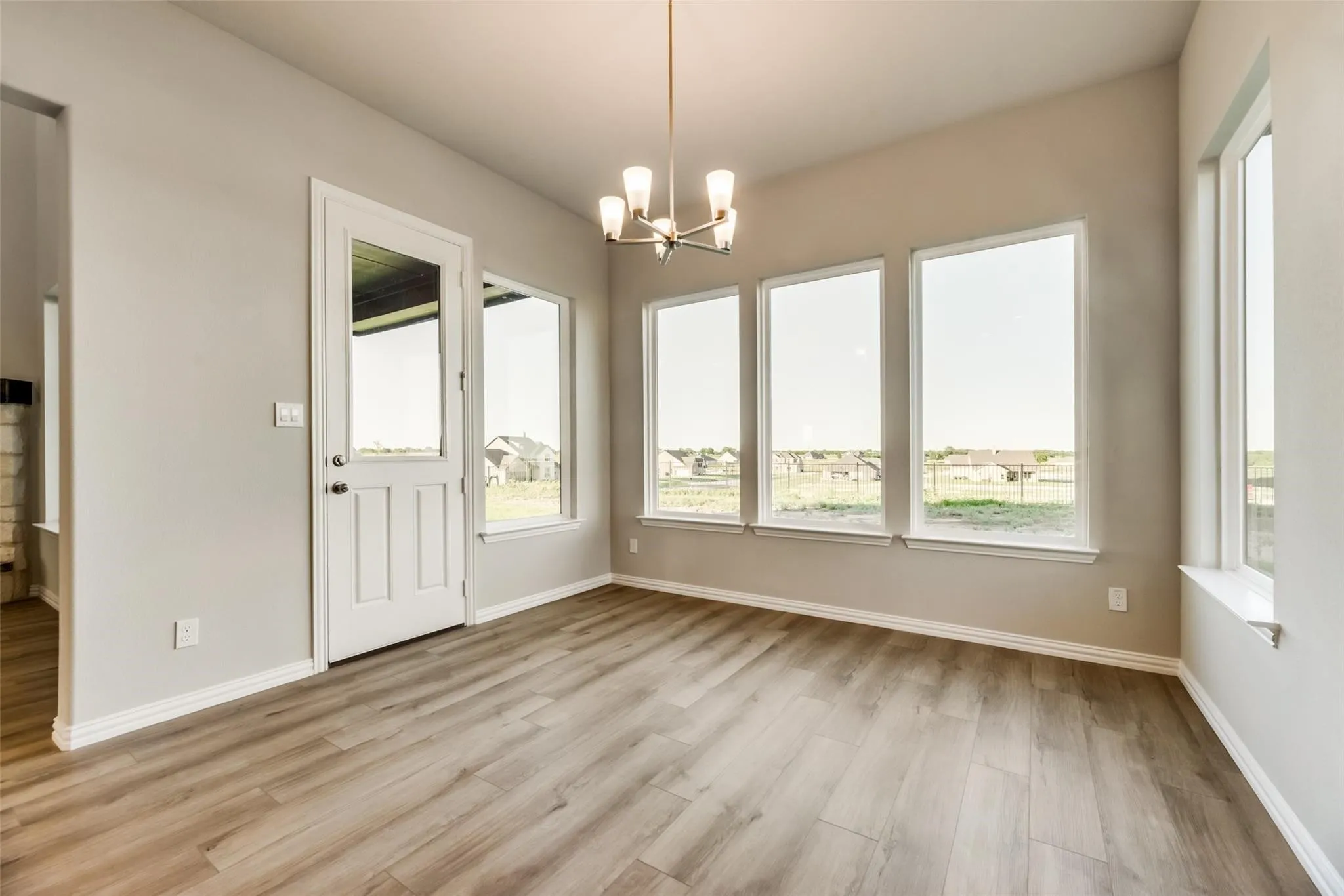 Wood-finish flooring, multiple large windows, glass-paneled door, and a decorative ceiling light fixture