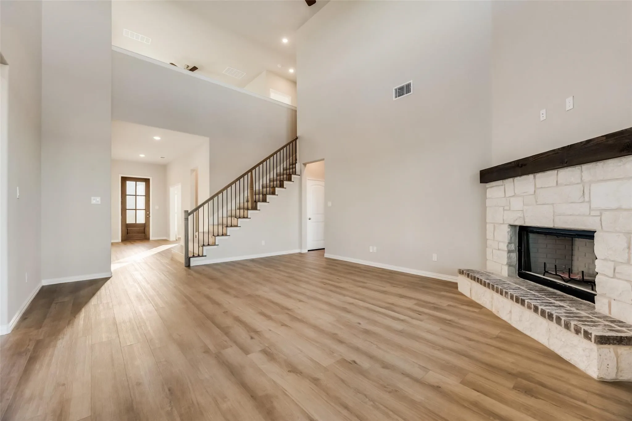 Two-story living area featuring a stone fireplace with a wood mantle, wood-finish flooring, and a staircase with dark wood handrails