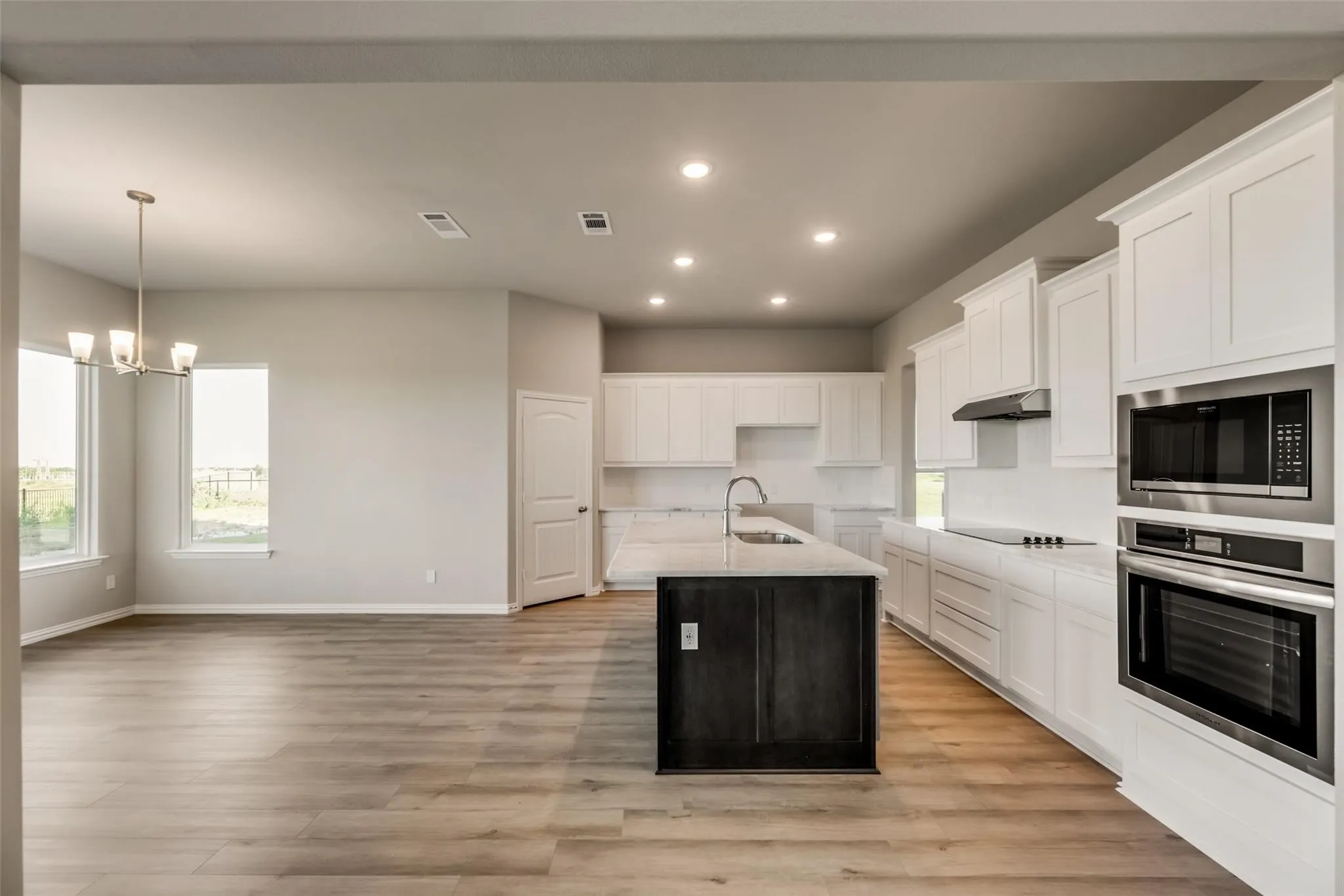Open-concept living area featuring wood-finish flooring, recessed lighting, a kitchen island with a sink, white cabinetry, and stainless steel appliances