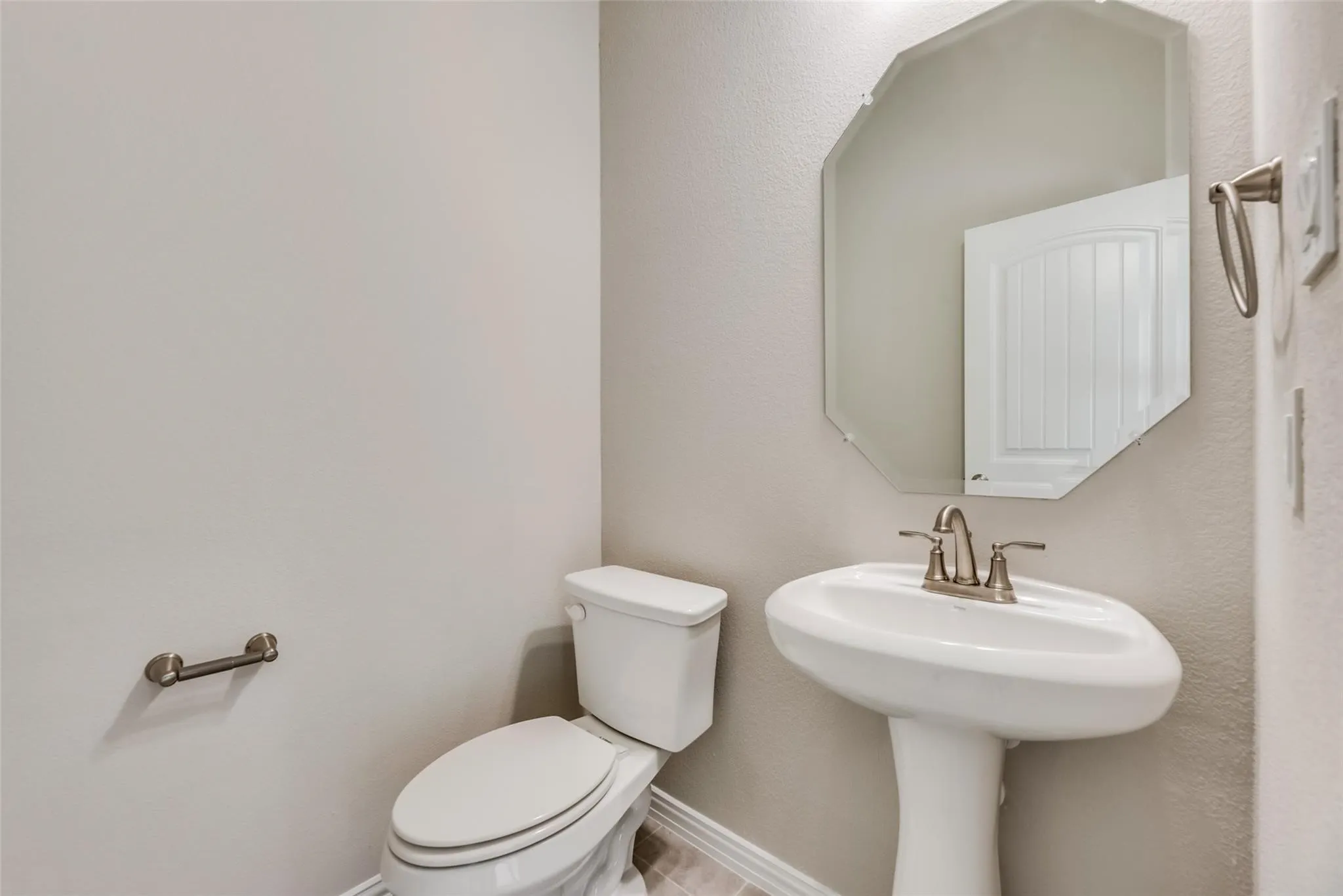 Pedestal sink with brushed nickel faucet, an octagonal mirror, and tile flooring