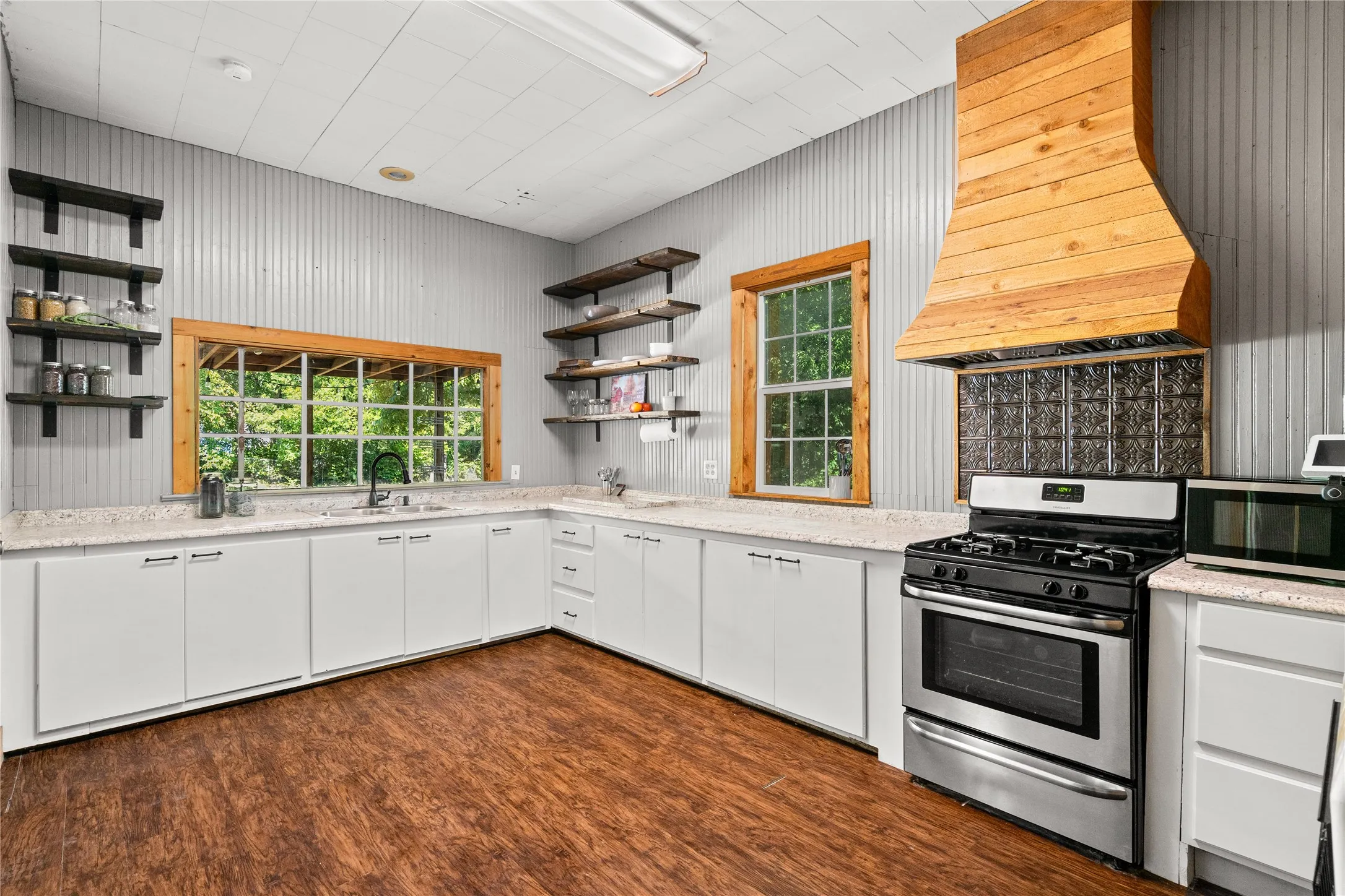 Kitchen featuring wood-finish flooring, white cabinetry, light-toned countertops, a stainless-steel range, and a custom wood range hood