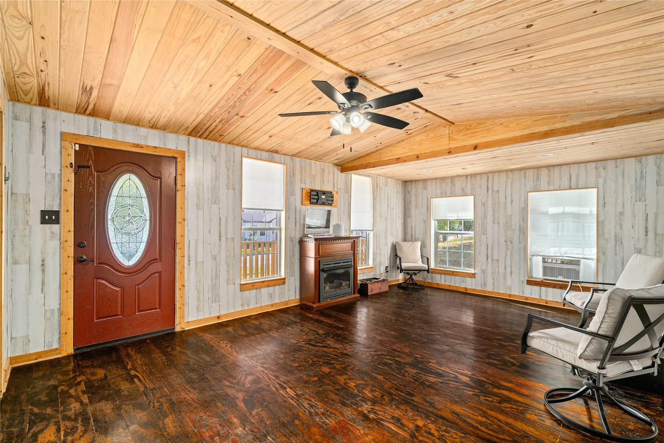 Vaulted wood-plank ceiling, wood-finish flooring, accent wall paneling, and a decorative front entry door with leaded glass