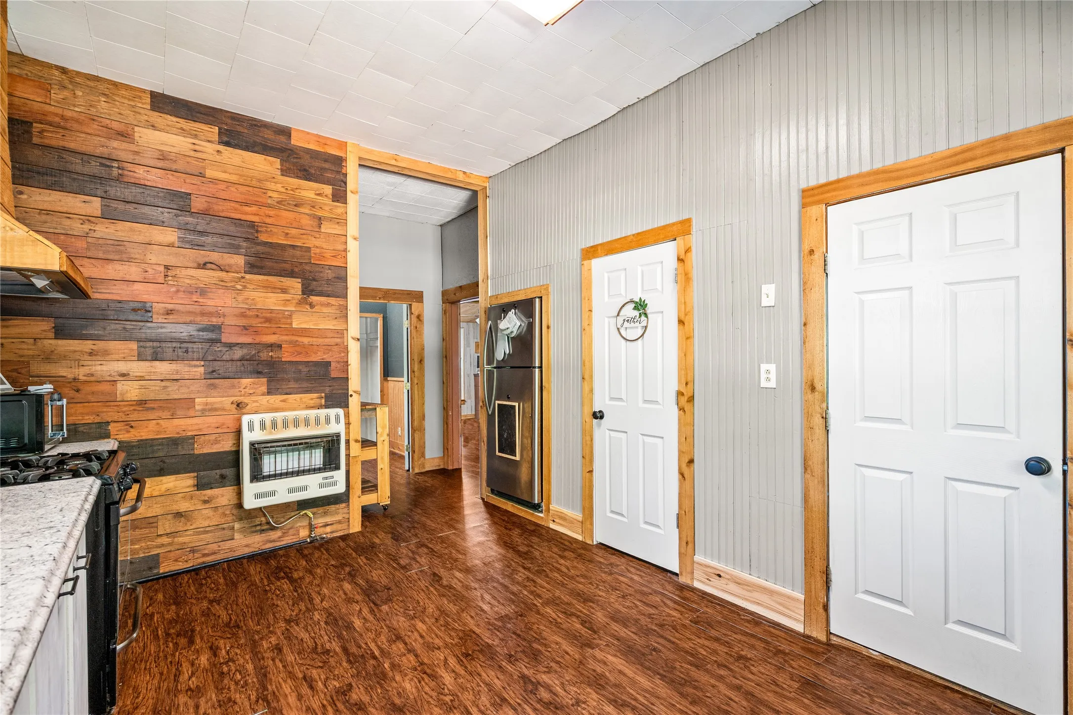 Wood-finish flooring, wood plank accent wall, built-in wall heater, paneled walls, and multiple interior doors with wood trim