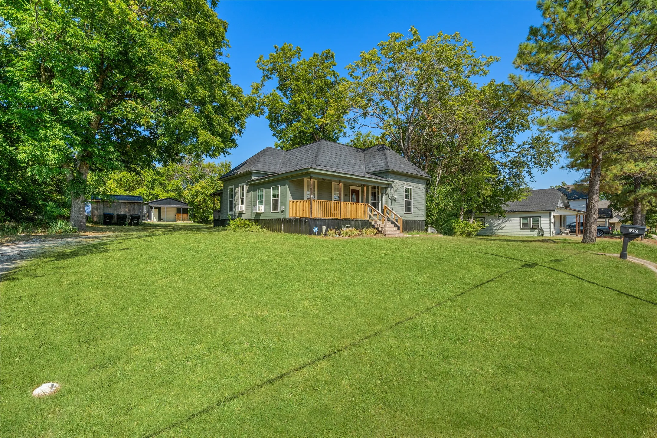 Expansive front lawn with mature trees and a gravel driveway