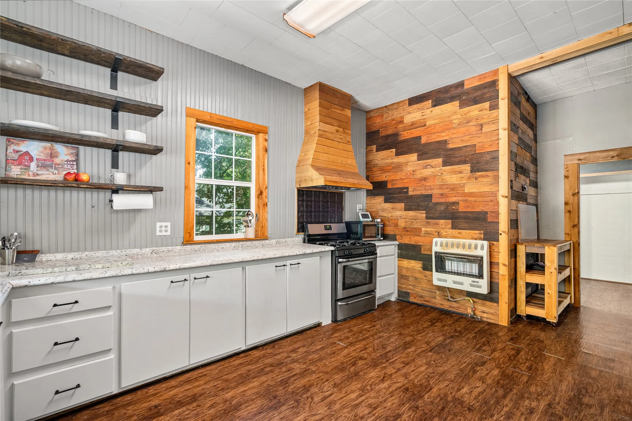 Wood-finish flooring, white cabinetry with dark hardware, light-toned countertops, and open shelving