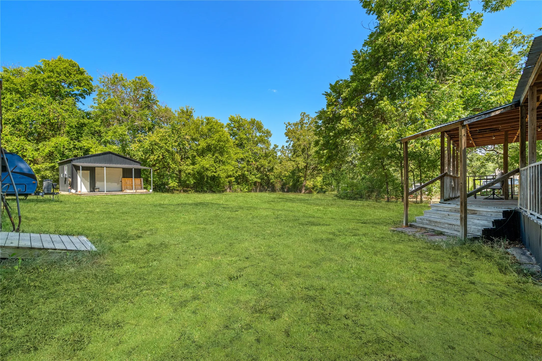 Expansive green lawn with mature trees and a detached structure featuring a covered porch