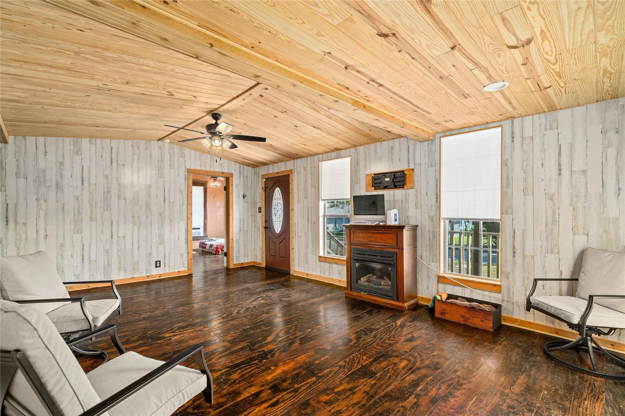 Wood-finish flooring, white wood paneling, wood-finish vaulted ceiling, ceiling fan, and a built-in fireplace