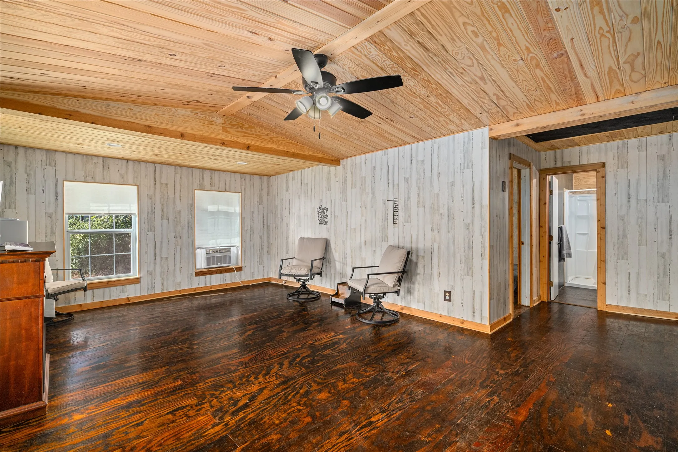 Vaulted wood-finish ceiling, dark wood-finish flooring, white wood-panel wall finish, and two windows with exterior views