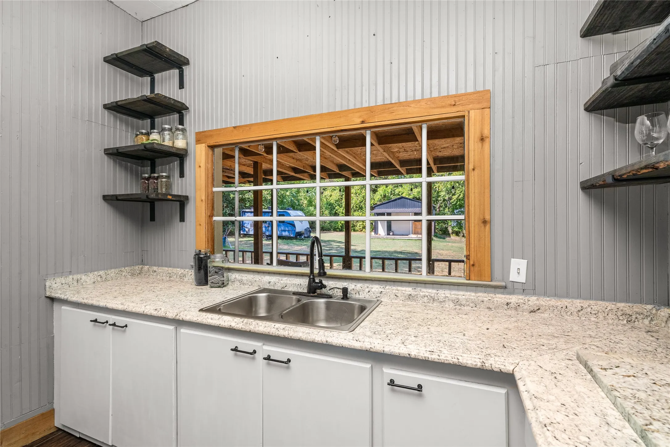 White cabinetry with black hardware, double basin sink with black faucet, light-toned countertop, and wood-framed window with grid inserts