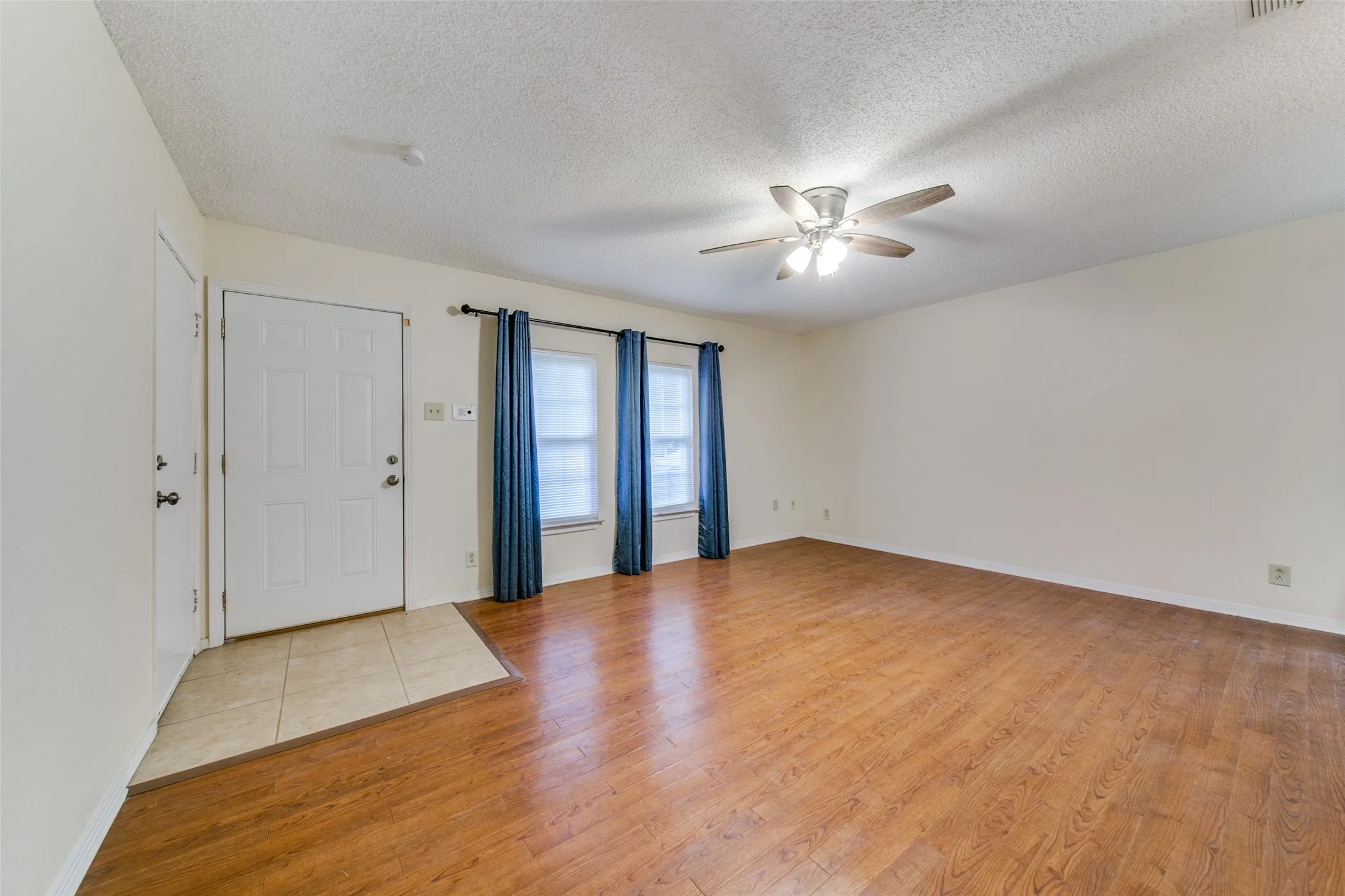 Expansive room with wood-finish flooring, a ceiling fan with integrated lighting, and dual windows