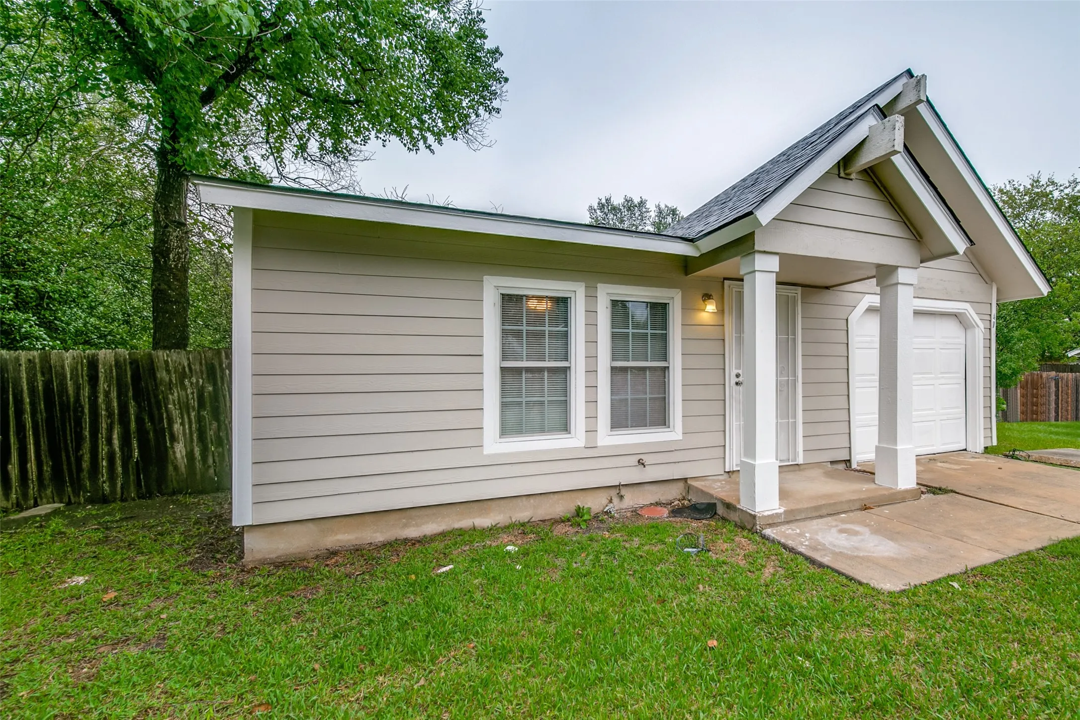 Light-colored horizontal siding, white trim windows, covered entry with white columns, attached garage with white door, and green lawn