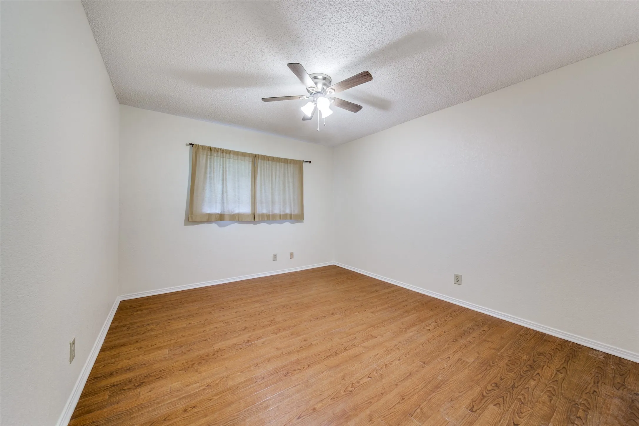 Wood-finish flooring, white walls, and a ceiling fan with integrated lighting