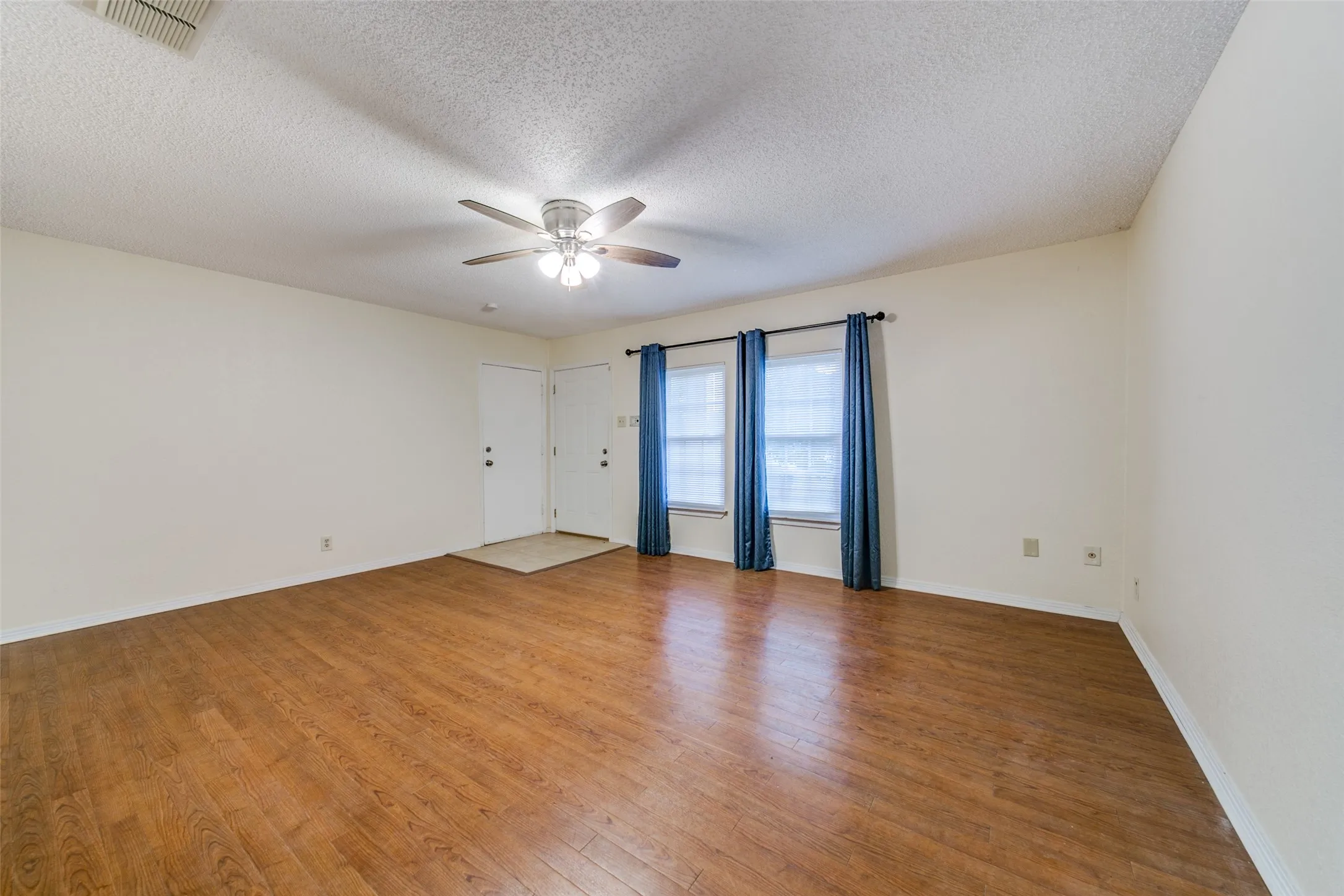 Wood-finish flooring throughout, ceiling fan with integrated lighting, two windows for natural light, and a white entry door
