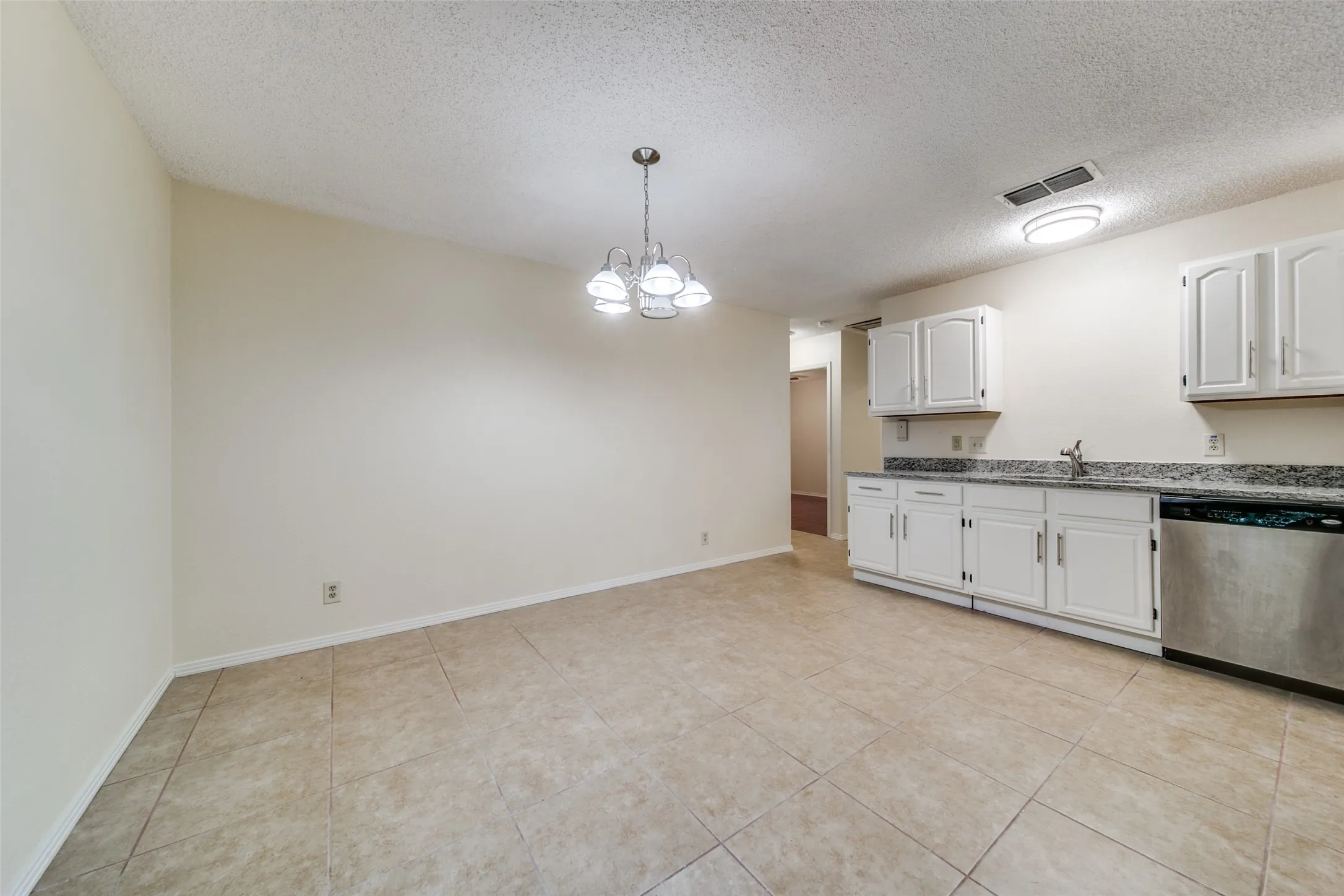 Recessed lighting in kitchen area, white cabinetry, granite-style countertops, stainless steel dishwasher, and neutral-toned tile flooring