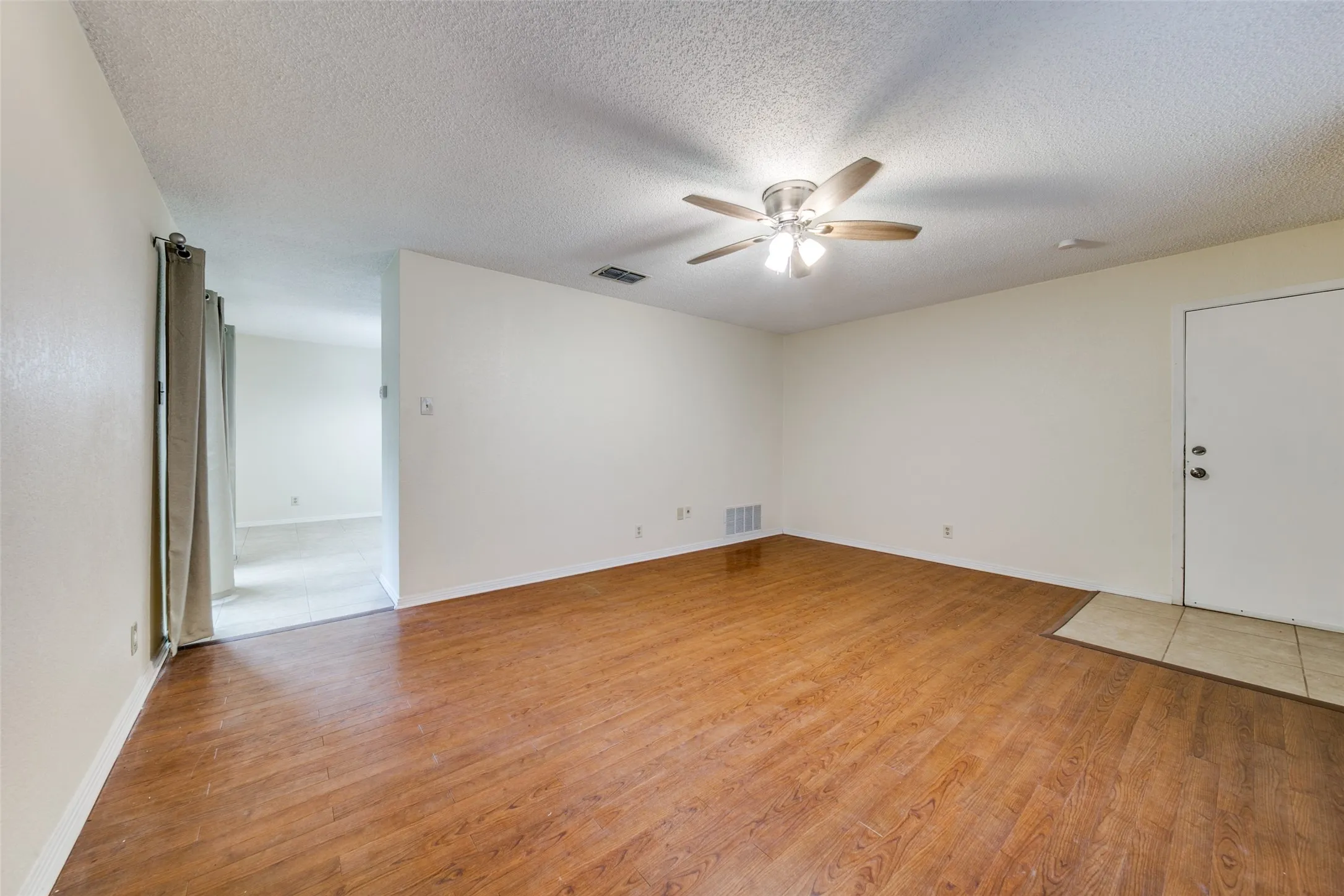 Spacious interior featuring wood-finish flooring, a ceiling fan with integrated lighting, and neutral wall tones