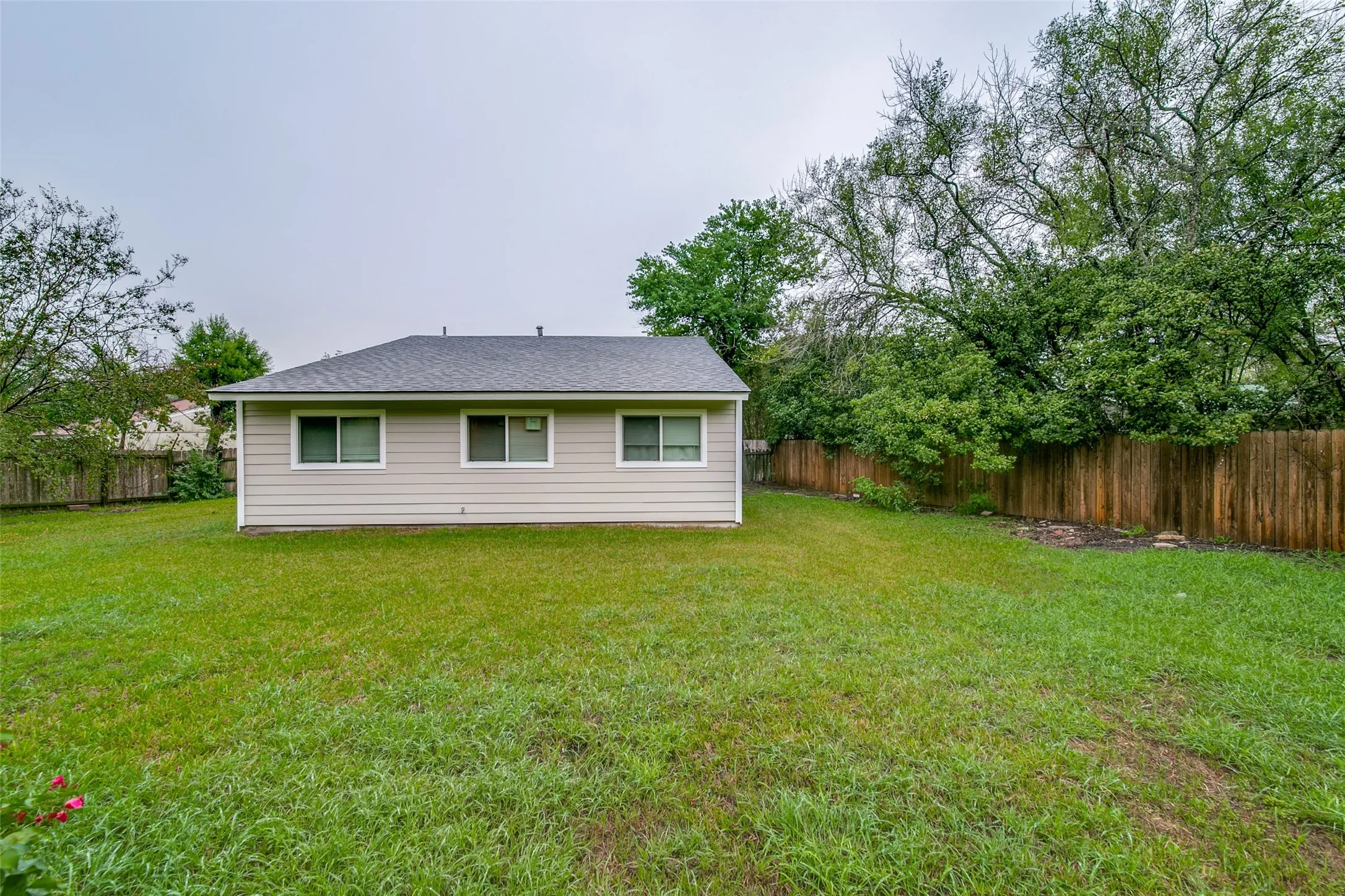 Expansive backyard featuring a manicured lawn, full perimeter wood fencing, and mature trees