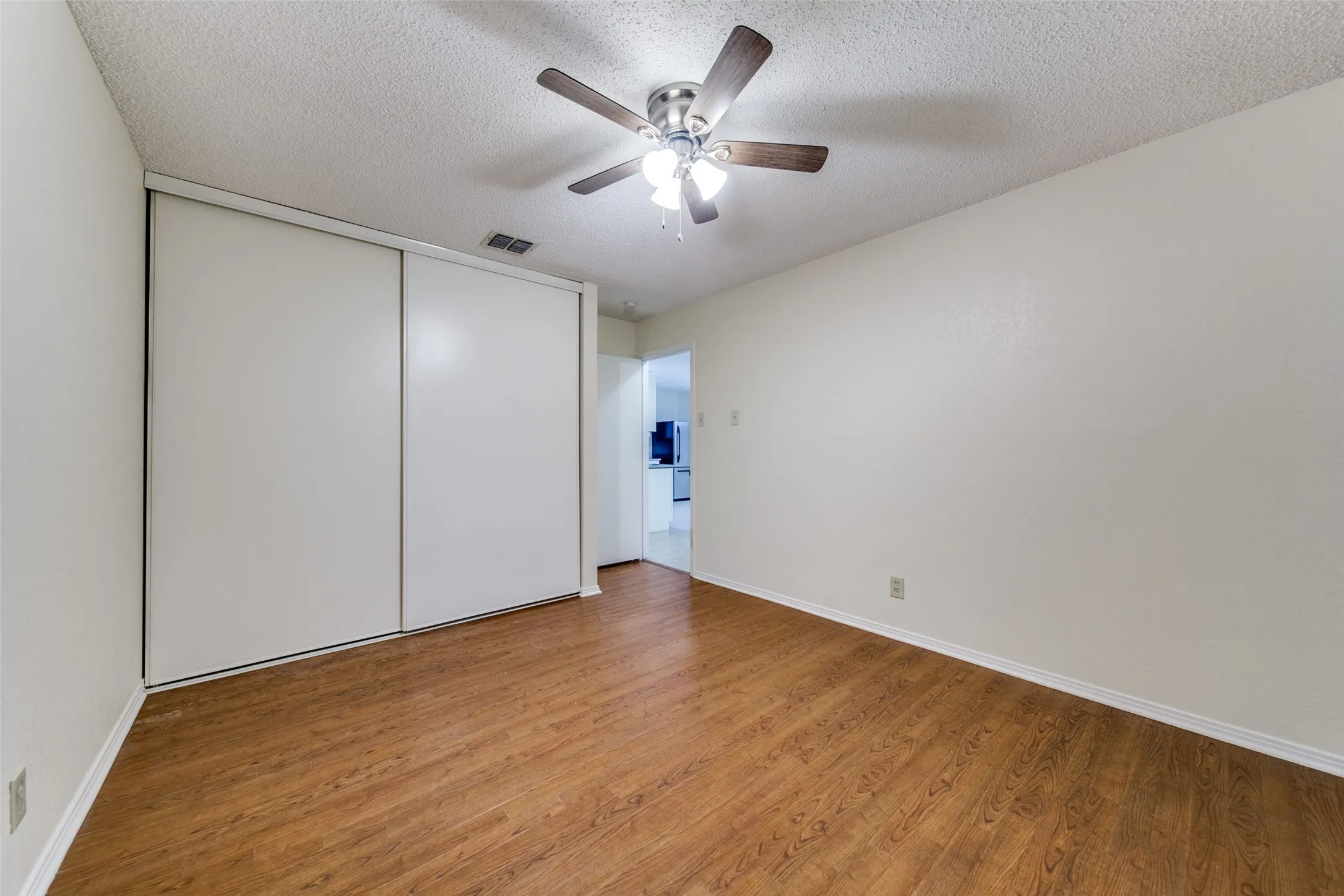 Wood-finish flooring, white walls, and a ceiling fan with integrated lighting