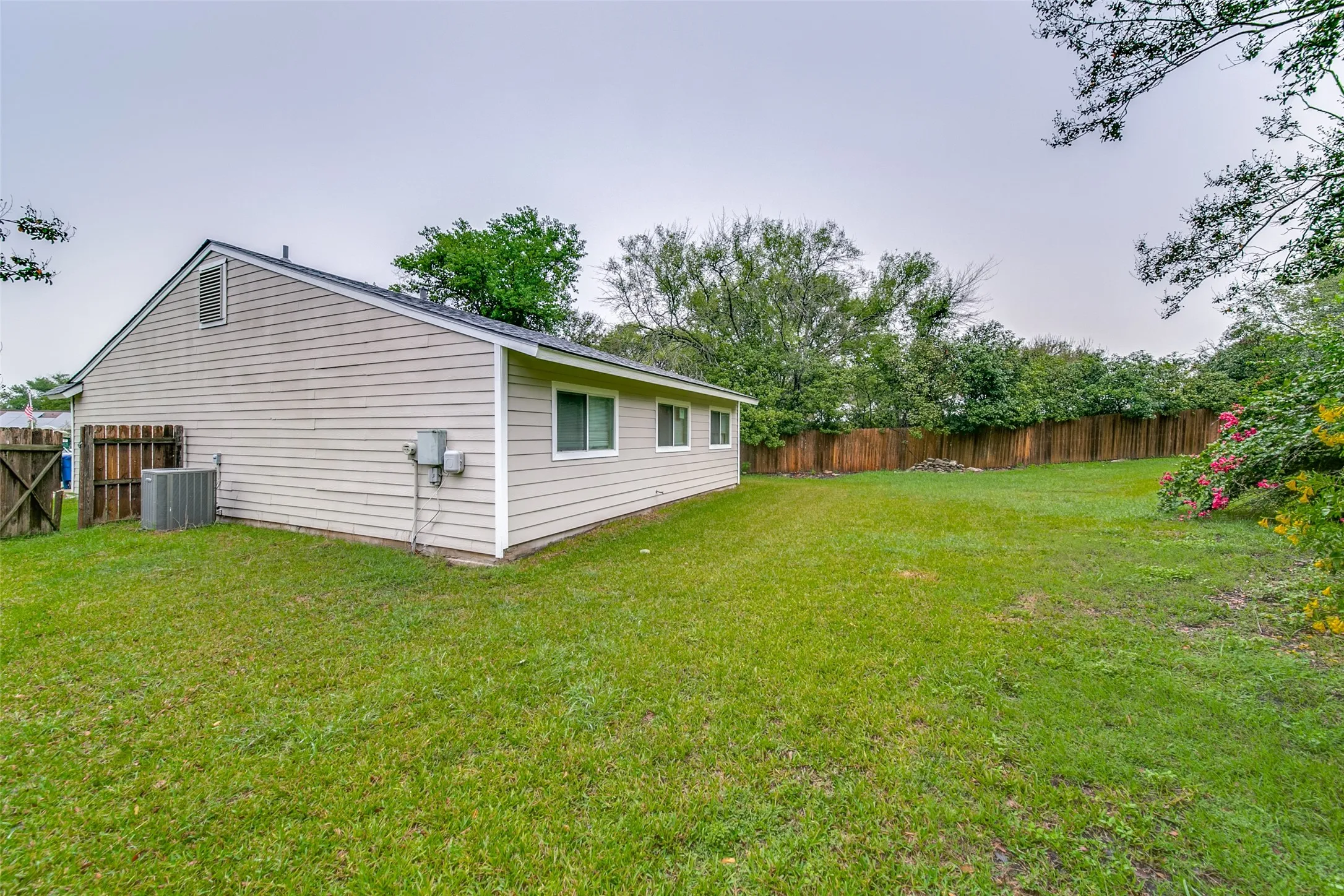 Expansive grassy yard with wood fencing and mature perimeter landscaping