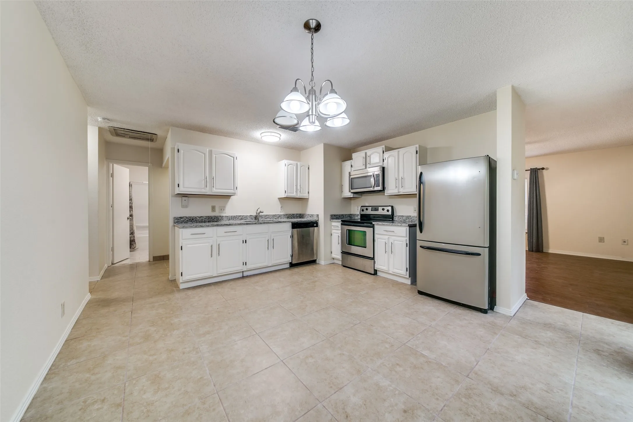 Kitchen featuring white cabinetry, stainless steel appliances, granite-style countertops, and tile flooring