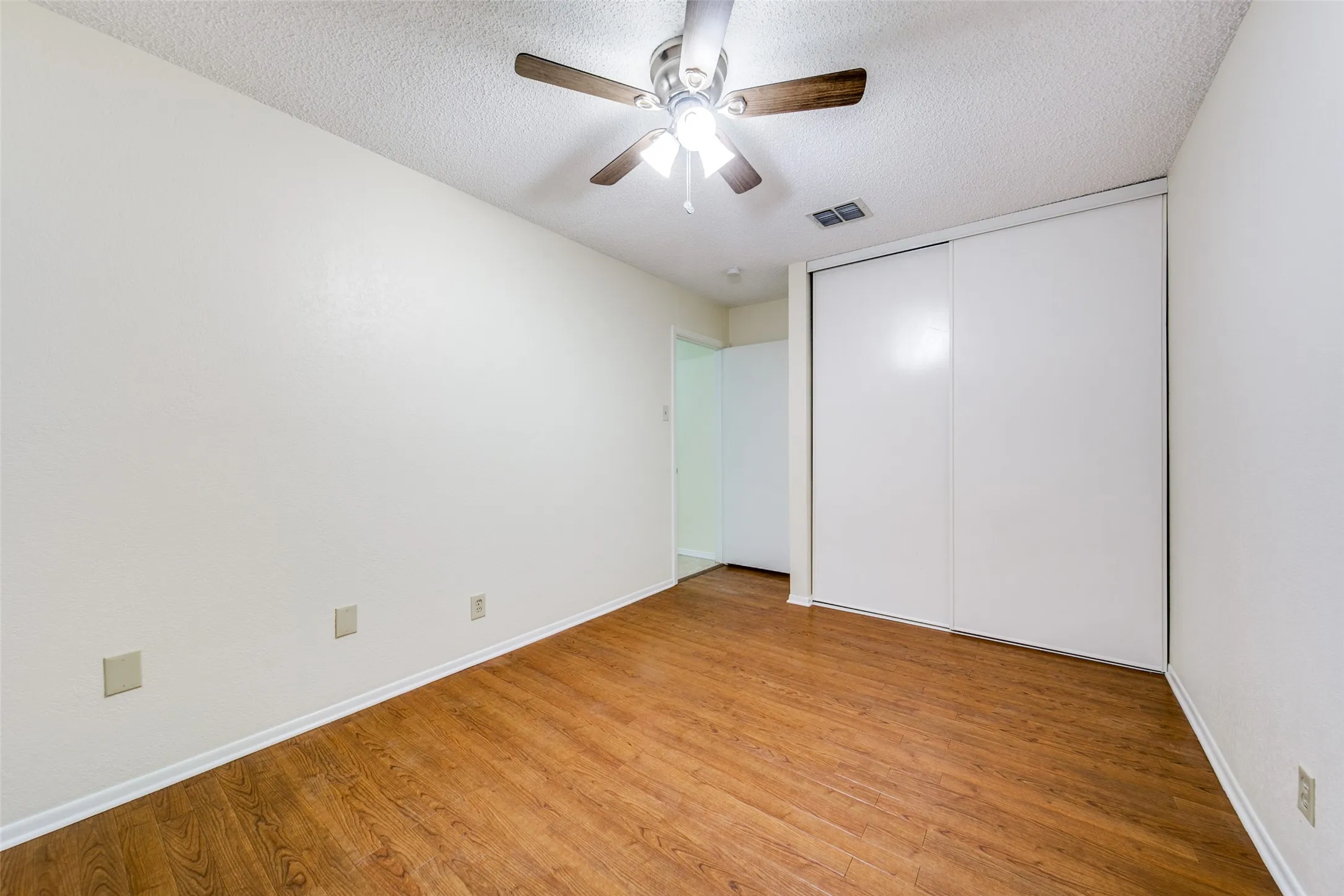 Wood-finish flooring with white baseboards, a ceiling fan with integrated lighting, and a closet with sliding doors