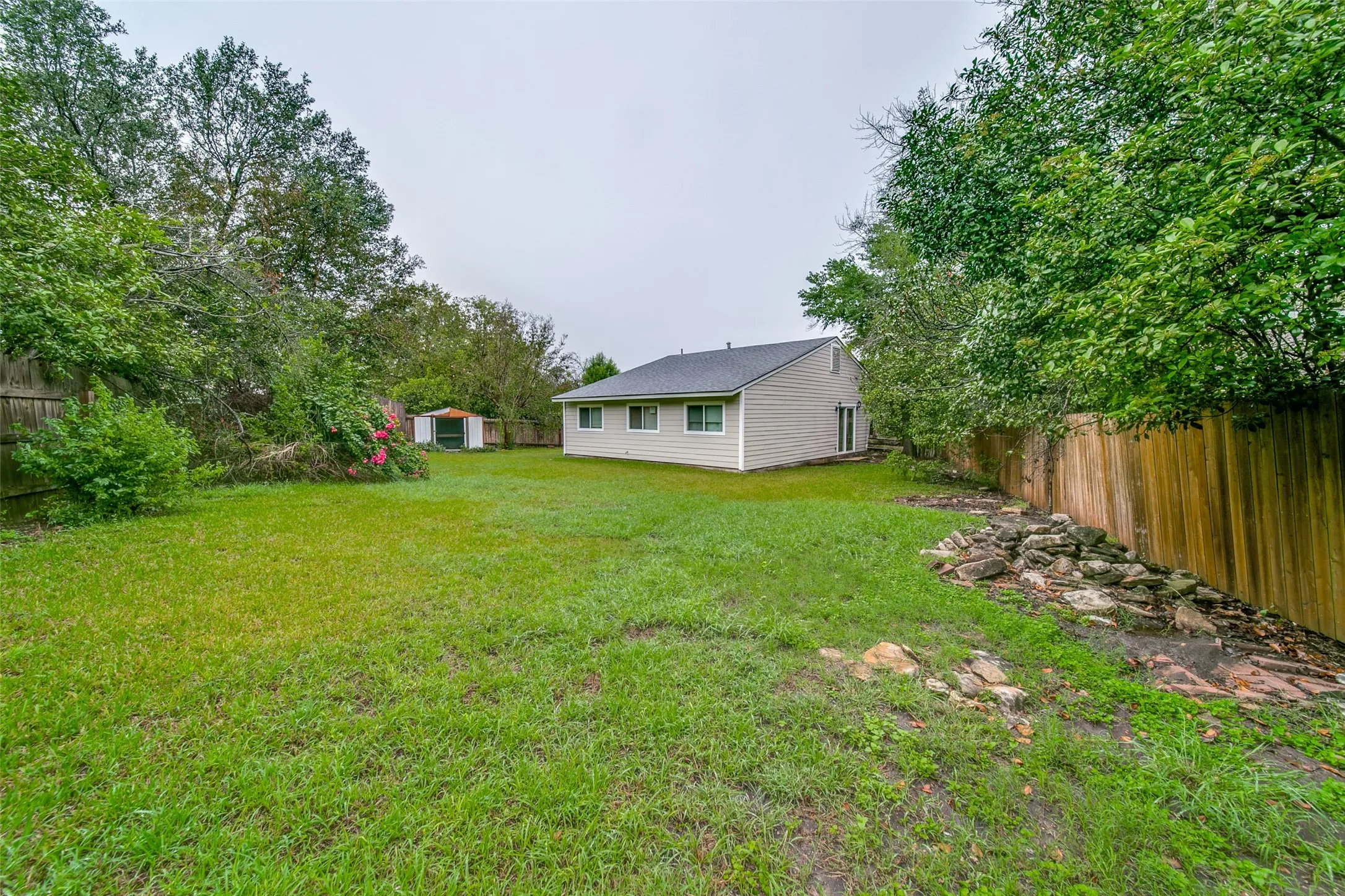 Expansive rear yard featuring green lawn, a wood fence, and mature trees