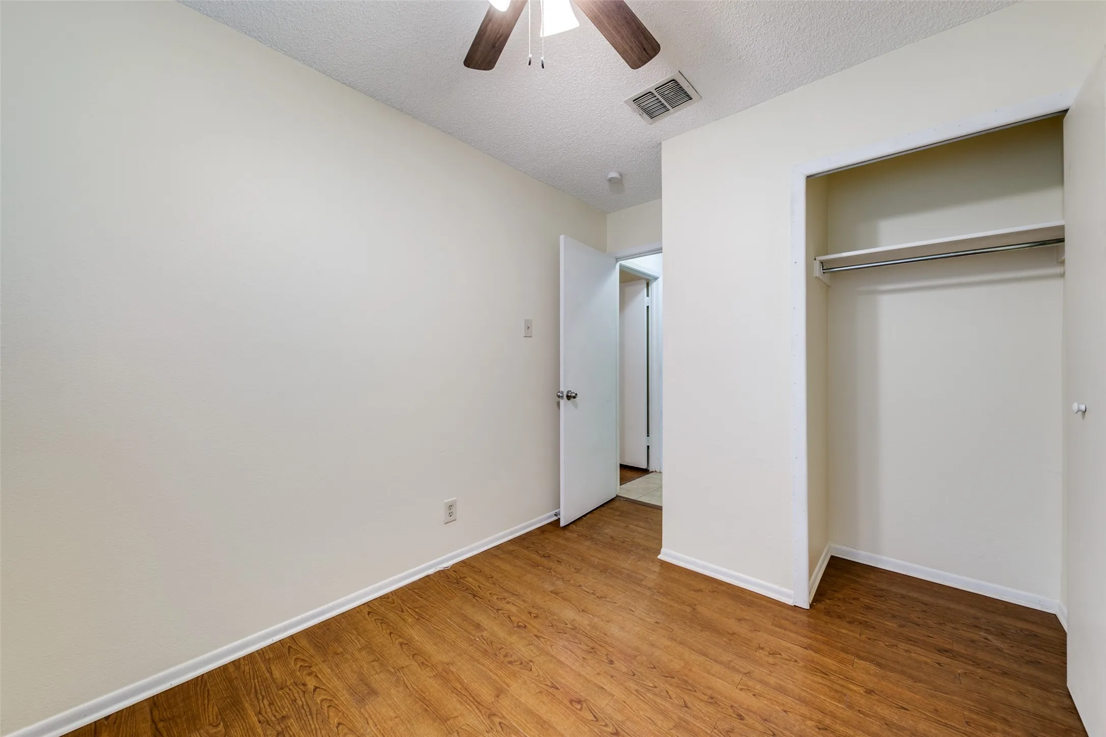 Wood-finish flooring, ceiling fan, and a built-in closet with hanging rod