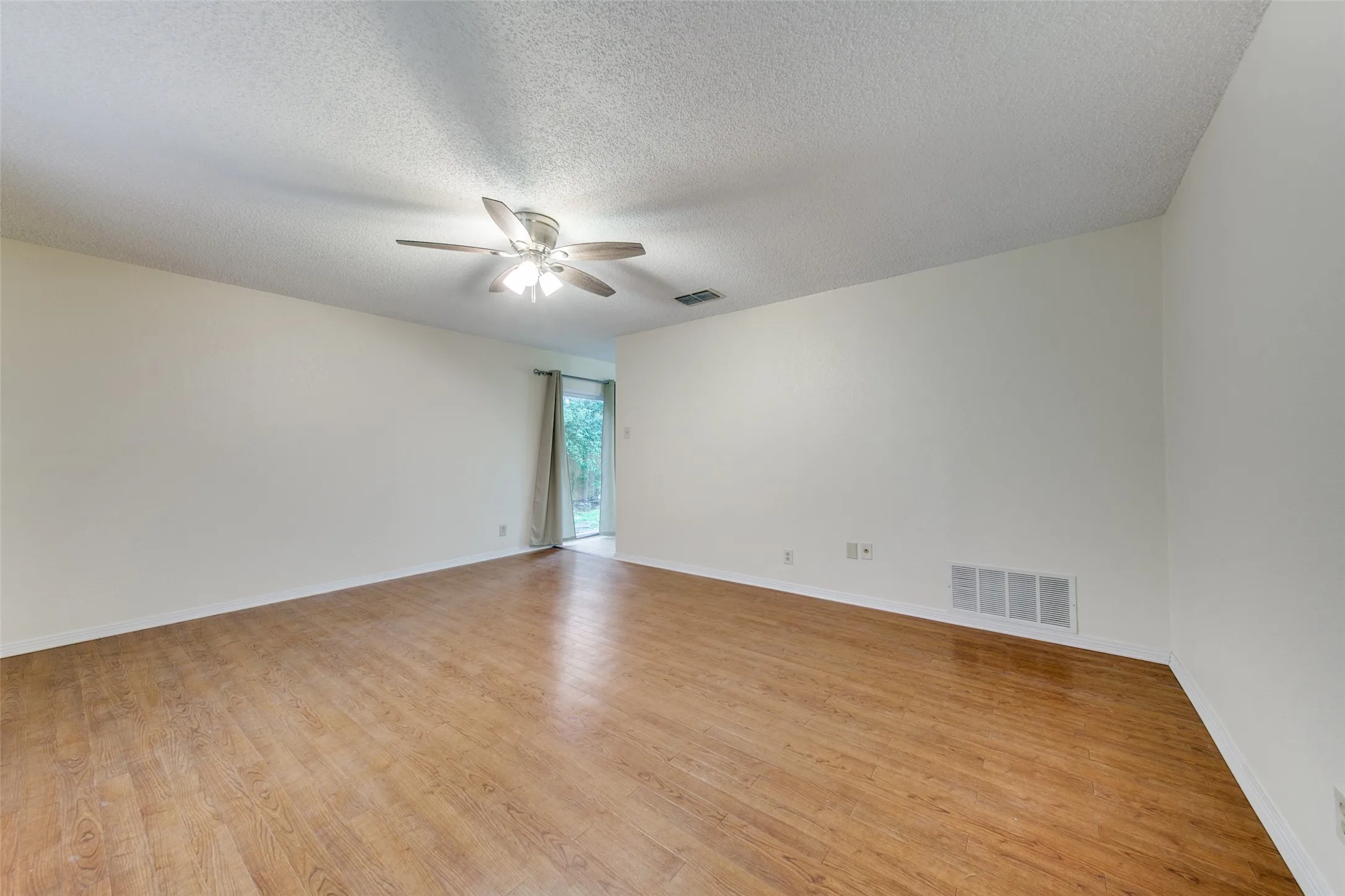 Spacious room with wood-finish flooring, neutral paint, and a ceiling fan with integrated lighting