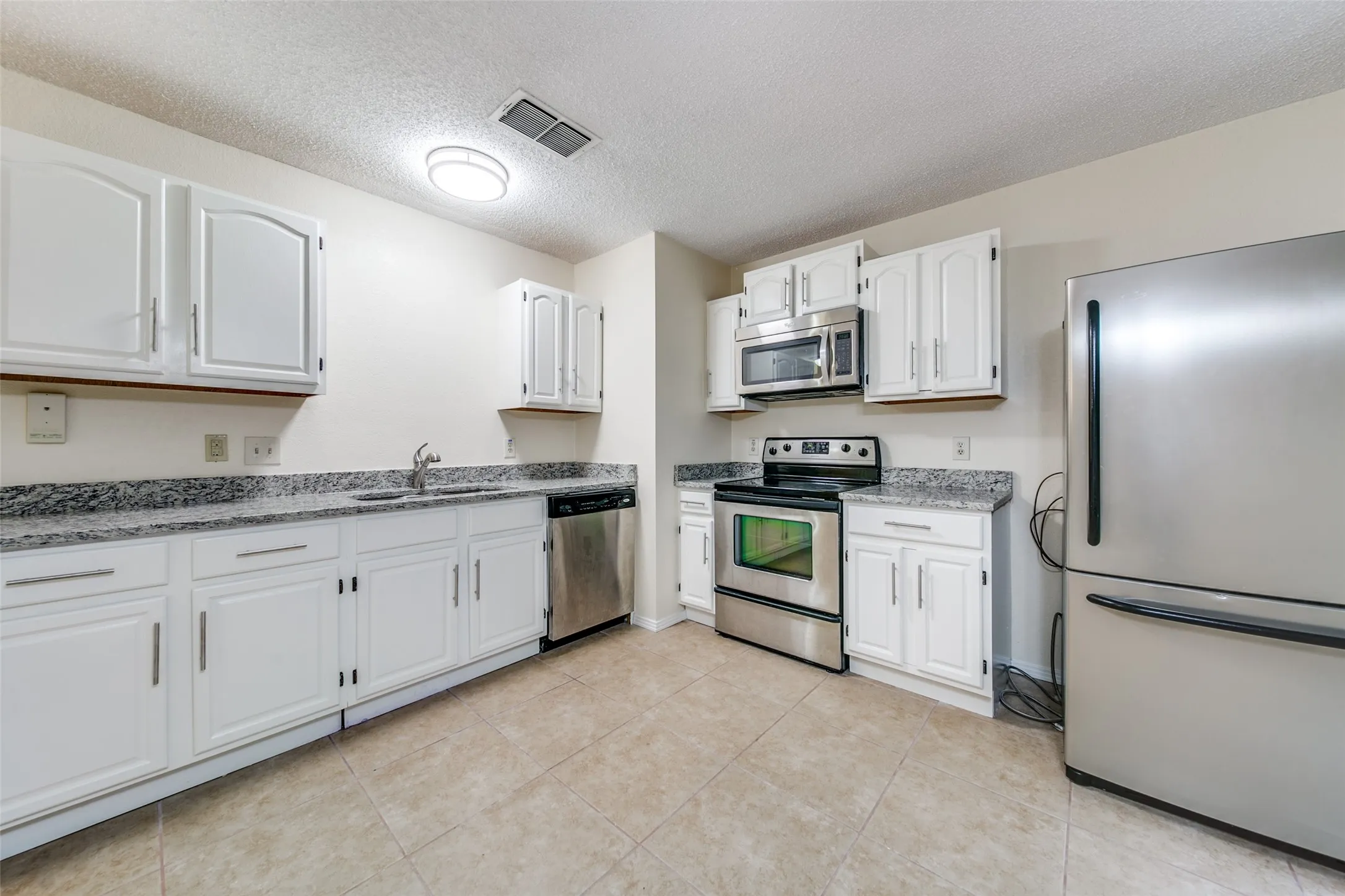 Kitchen featuring white cabinetry, stone countertops, stainless steel appliances, and tile flooring