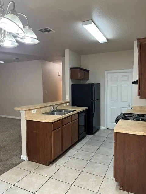 Kitchen featuring a breakfast bar, wood-finish cabinetry, tile flooring, and a double basin sink
