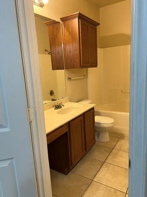 Vanity with integrated sink, wood-finish cabinetry, tile flooring, bathtub with shower, and wall-mounted storage cabinet