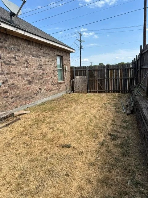 Brick exterior, shingled roof, single window, wood fencing, and metal gate