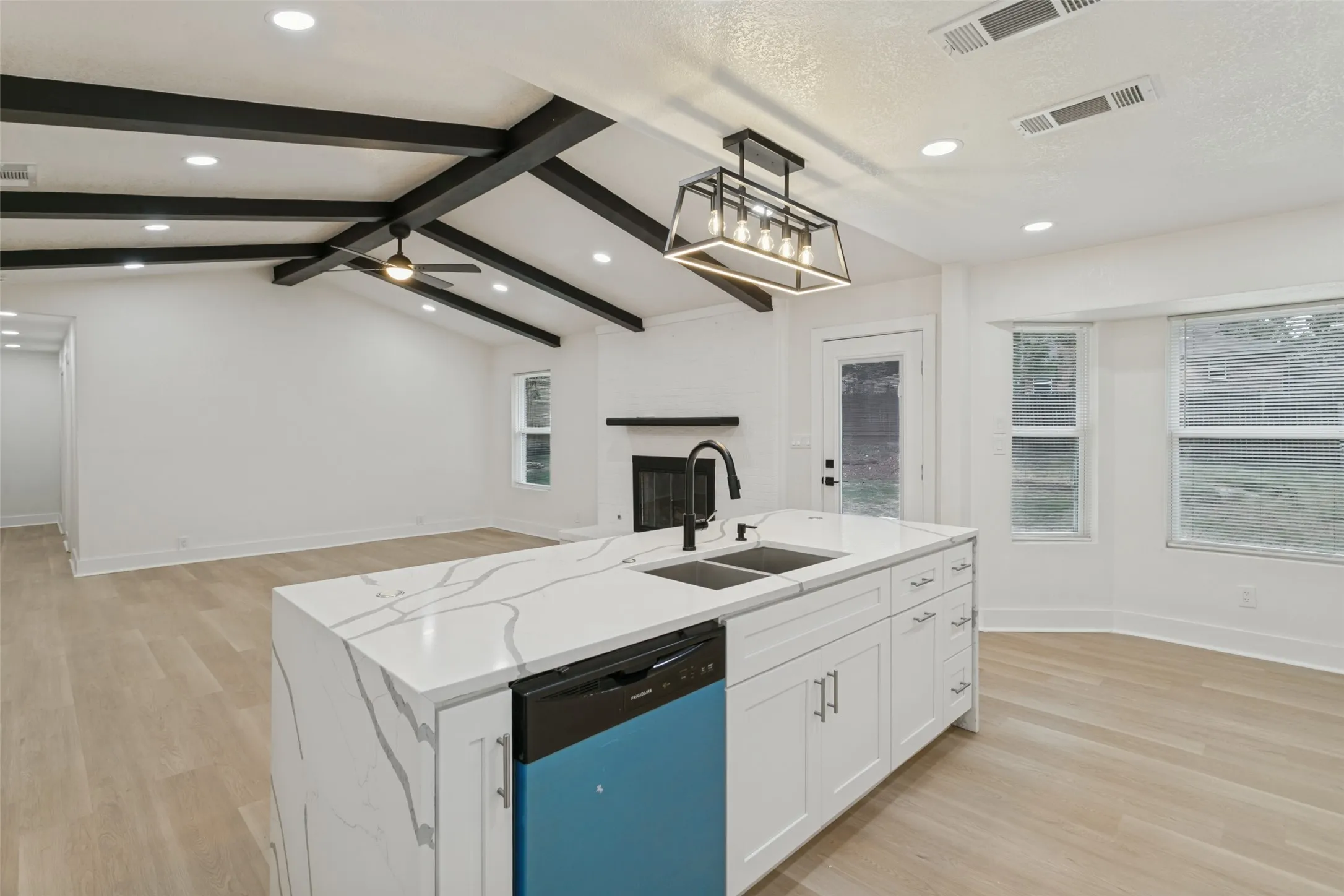 Vaulted ceilings with exposed beams, wood-finish flooring, kitchen island with integrated sink, recessed lighting, and a modern fireplace