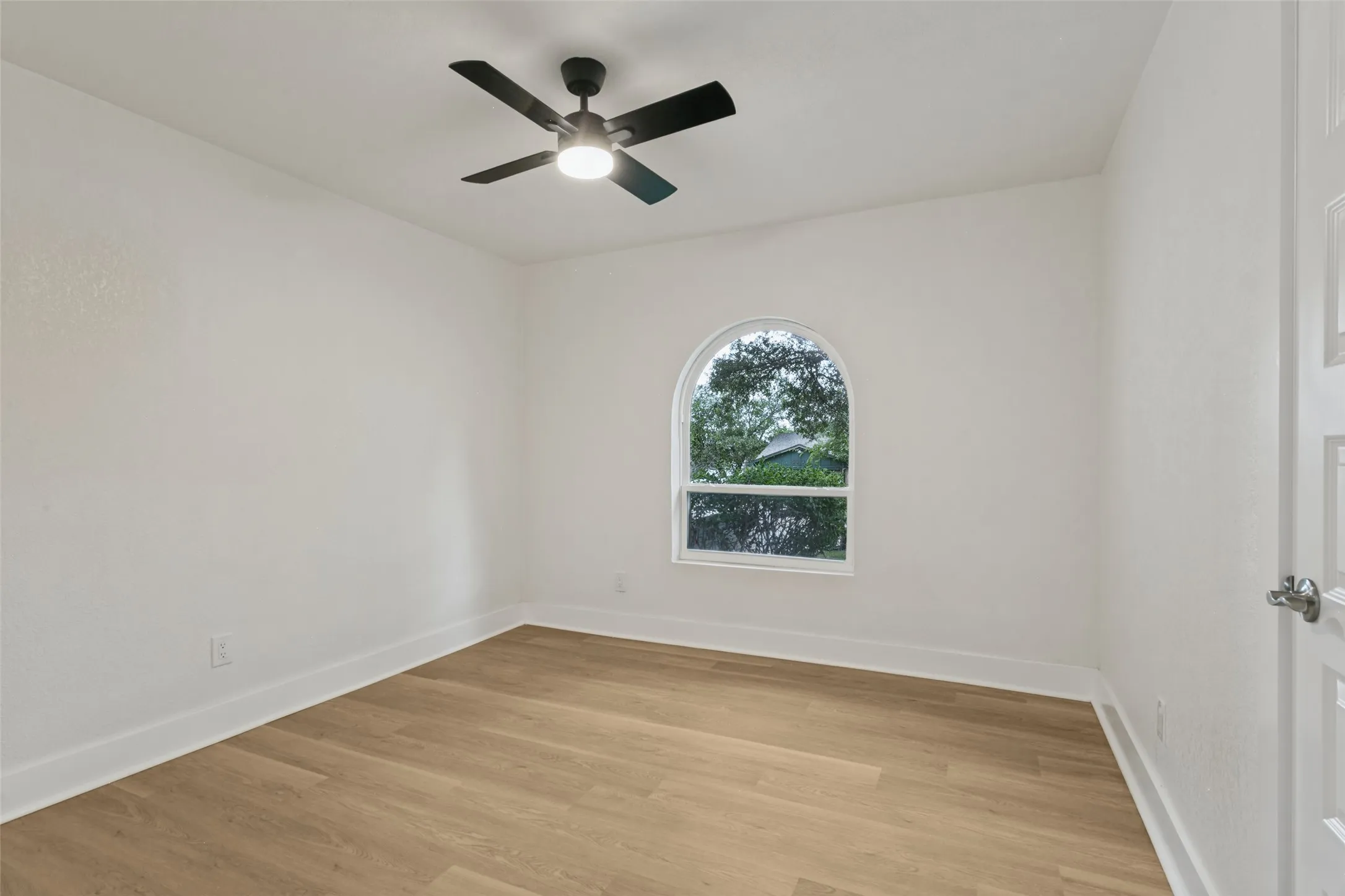 Wood-finish flooring, white walls, arched window, and a ceiling fan with light fixture