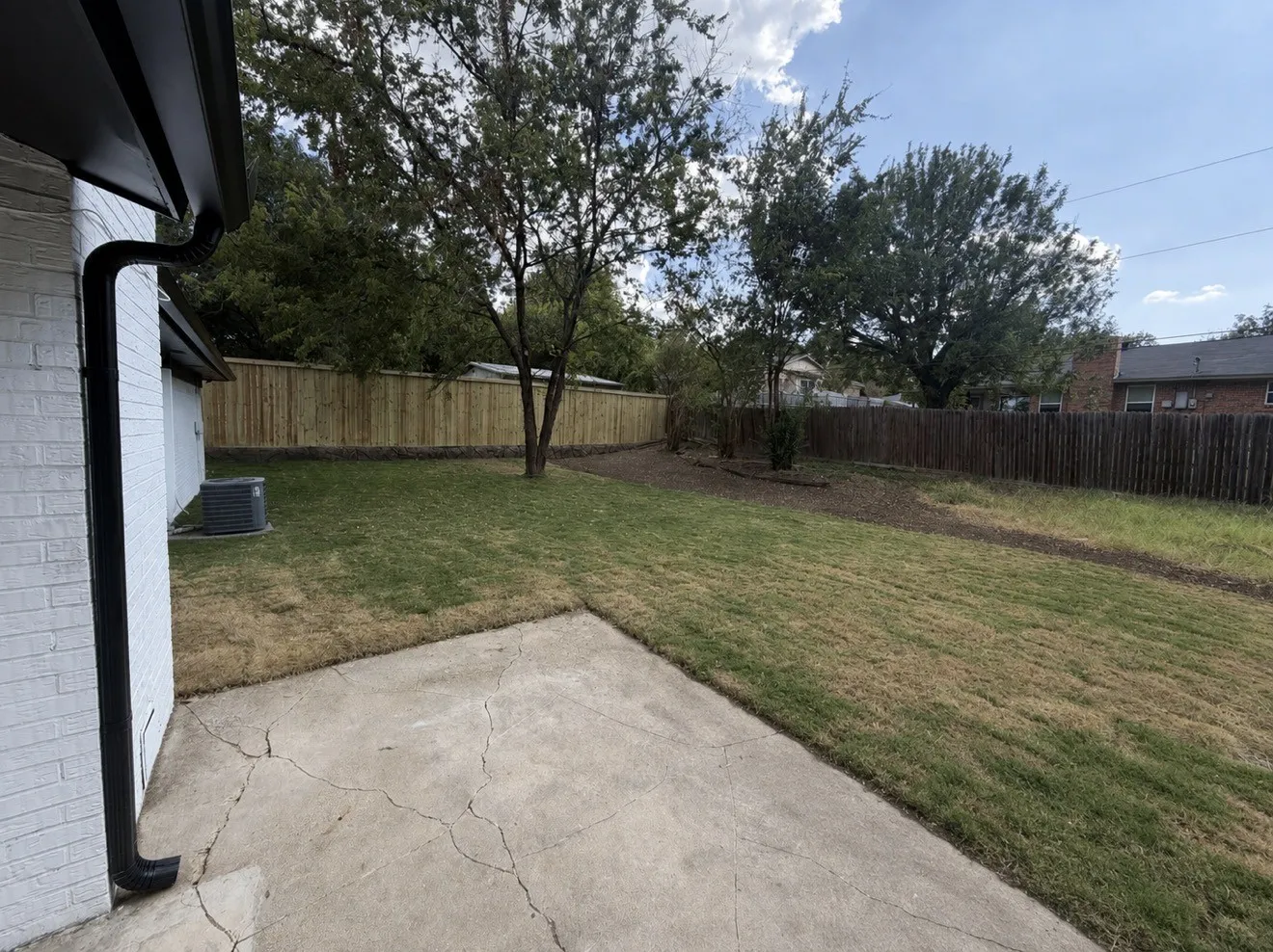Expansive grassy area with a partial privacy fence and mature trees