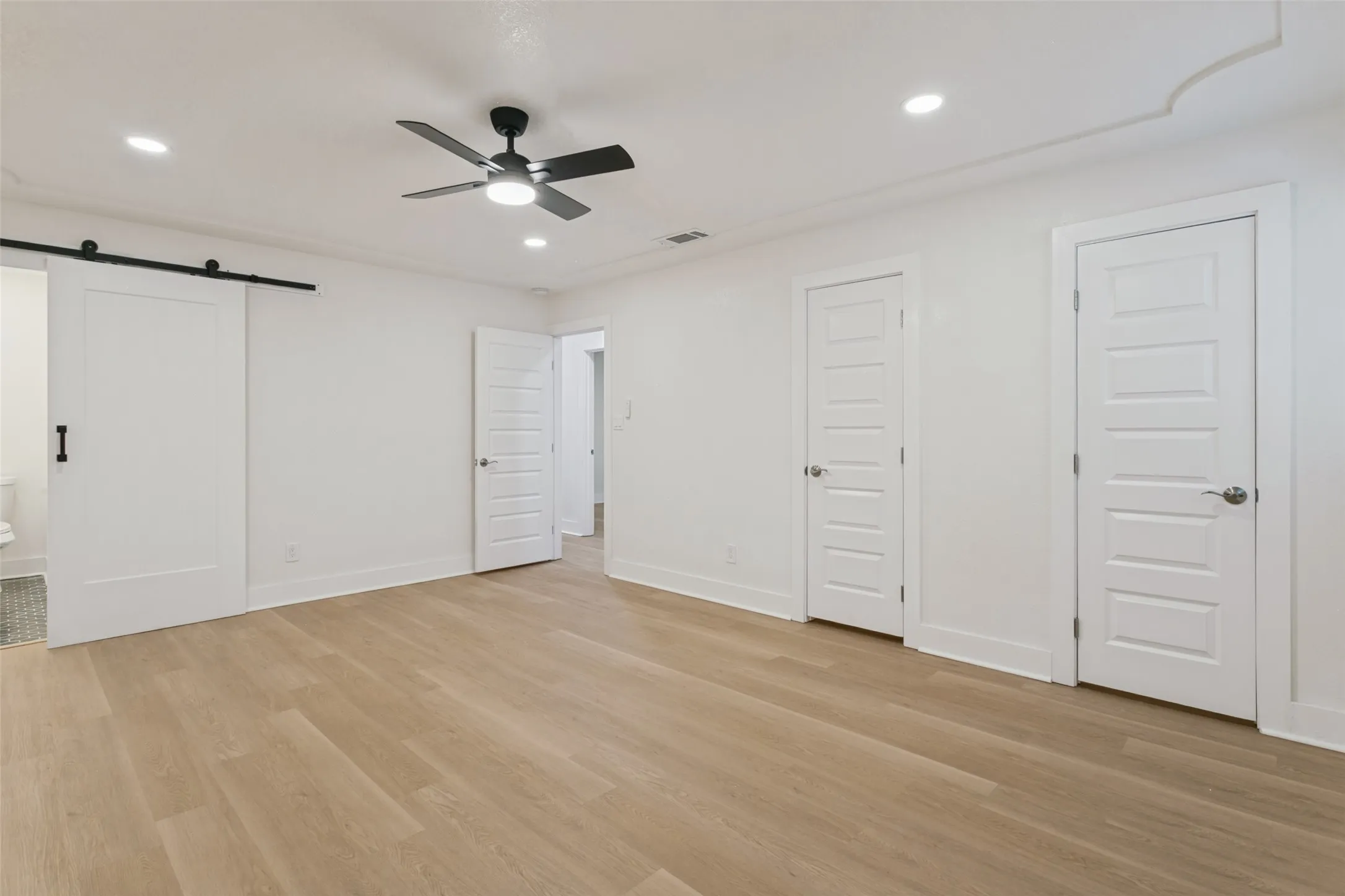 Light wood-finish flooring, recessed lighting, ceiling fan, and white panel doors