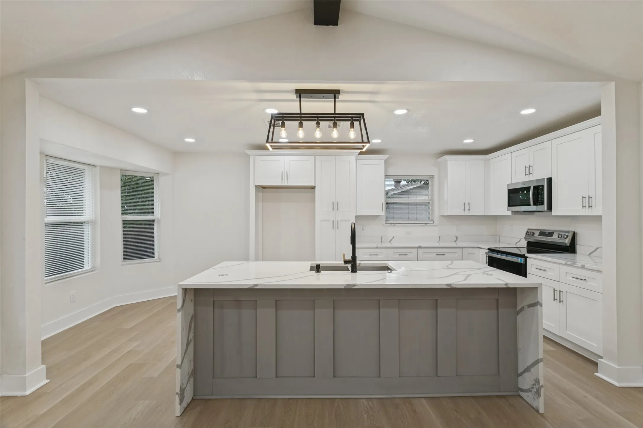 Kitchen featuring white cabinetry, a central island with a waterfall countertop, wood-finish flooring, recessed lighting, and a stainless steel appliance suite
