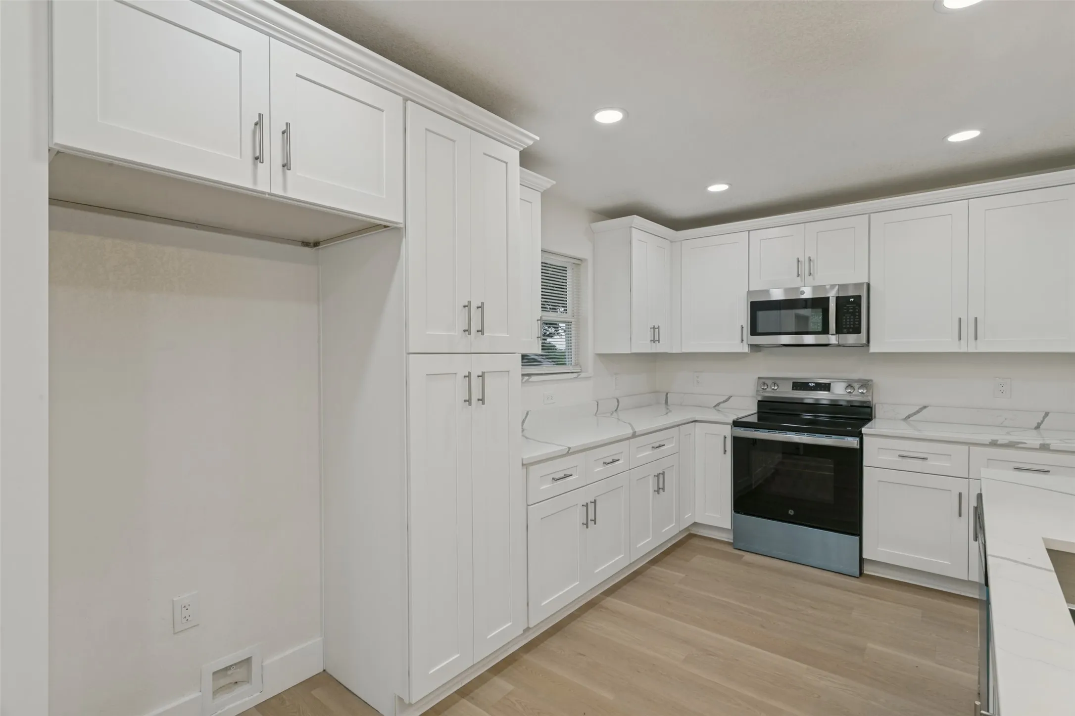 Kitchen with white shaker cabinetry, stainless steel appliances, light-toned wood-finish flooring, and recessed lighting