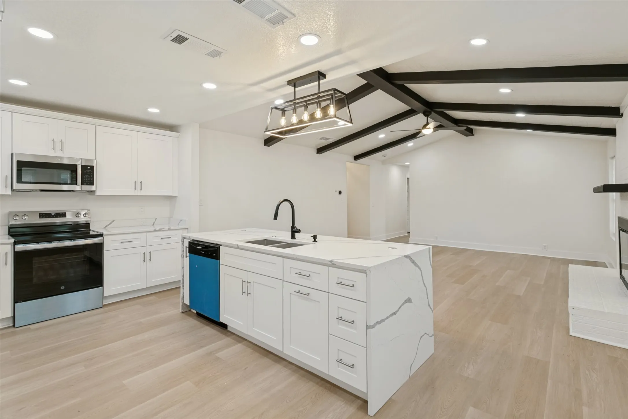 Kitchen island with an undermount sink, white cabinetry, integrated stainless steel appliances, wood-finish flooring, and a vaulted ceiling with exposed black beams